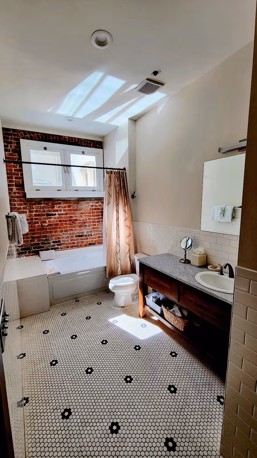 Bathroom with white hexagonal tile floor, brick accent wall behind bathtub, and wooden vanity in Hot Springs, Arkansas.