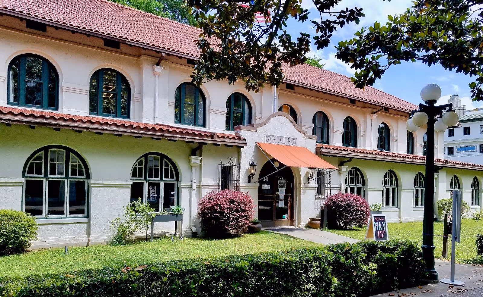 Two-story historic building with arched windows and red tile roof surrounded by green bushes in Hot Springs, Arkansas.