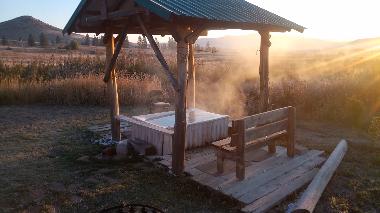 Steaming outdoor hot tub under a wooden pavilion at Big Medicine Hot Springs in Hot Springs, Montana during sunrise.