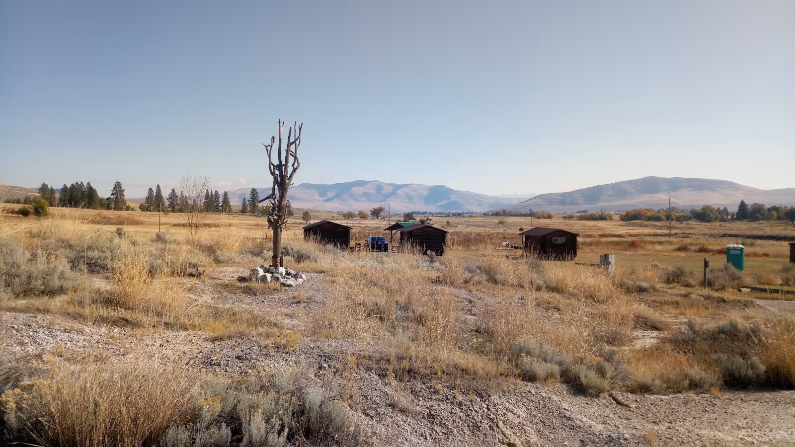 Wide view of dry grasslands with scattered cabins and distant mountains near Big Medicine Hot Springs in Hot Springs, Montana.