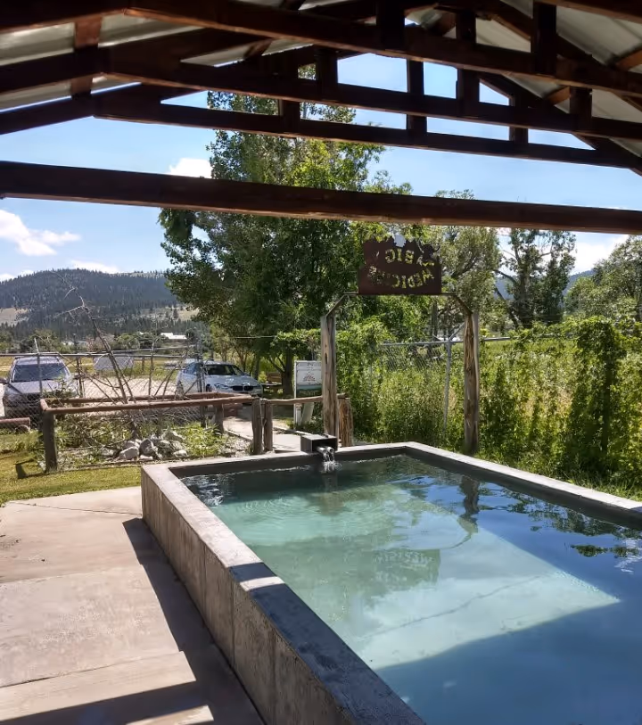 Small rectangular soaking pool with clear water under a shaded structure at Big Medicine Hot Springs, Montana.