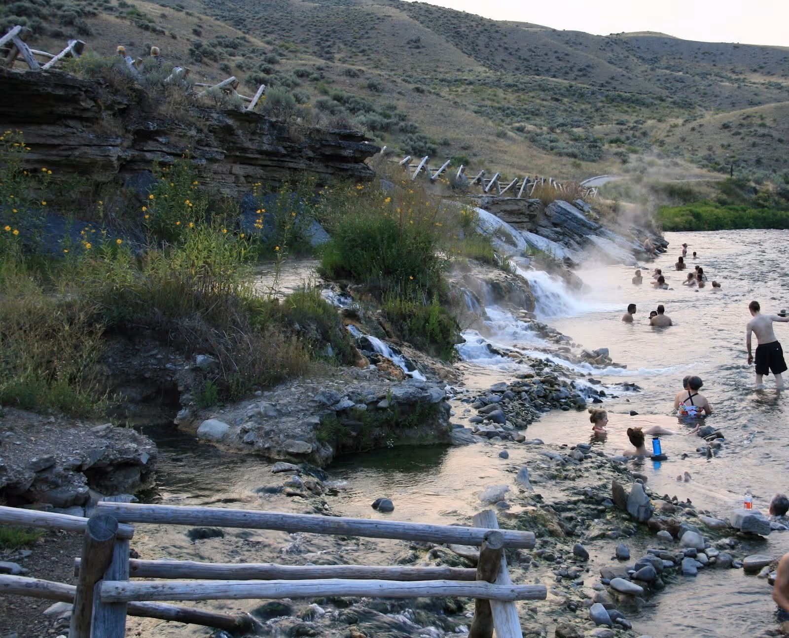 Visitors walking and soaking in rock-lined natural pools beside a flowing river at Boiling River Hot Springs near Gardiner Montana.