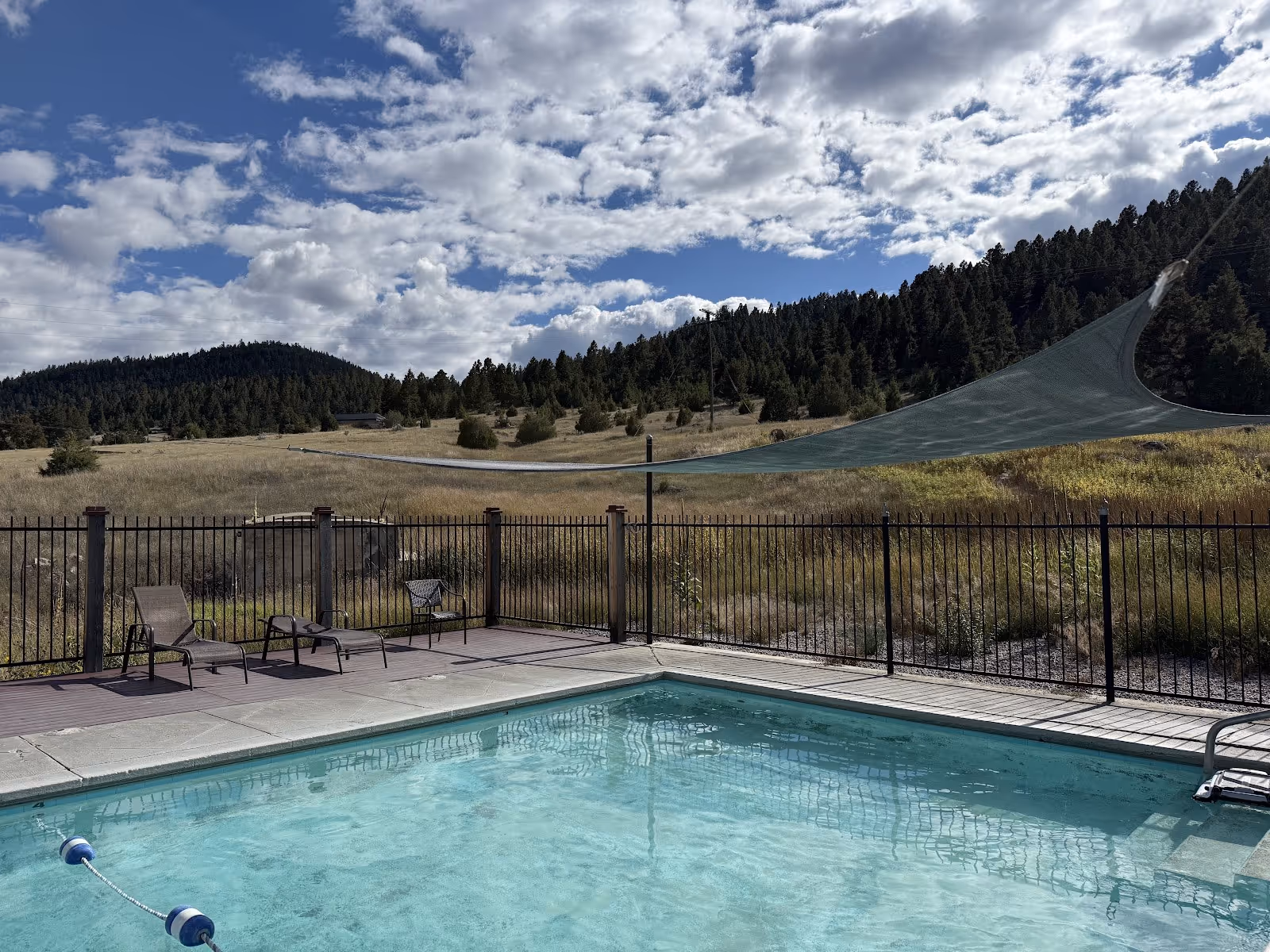 Clear soaking pool at Boulder Hot Springs surrounded by fencing and chairs with hills and trees in the natural background near Boulder Mont.