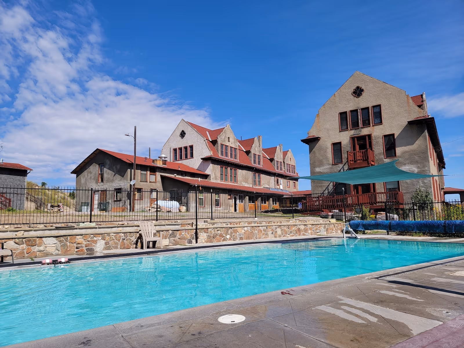 Outdoor mineral pool at Boulder Hot Springs with clear blue water and historic beige buildings under a bright sky in Boulder Montana.