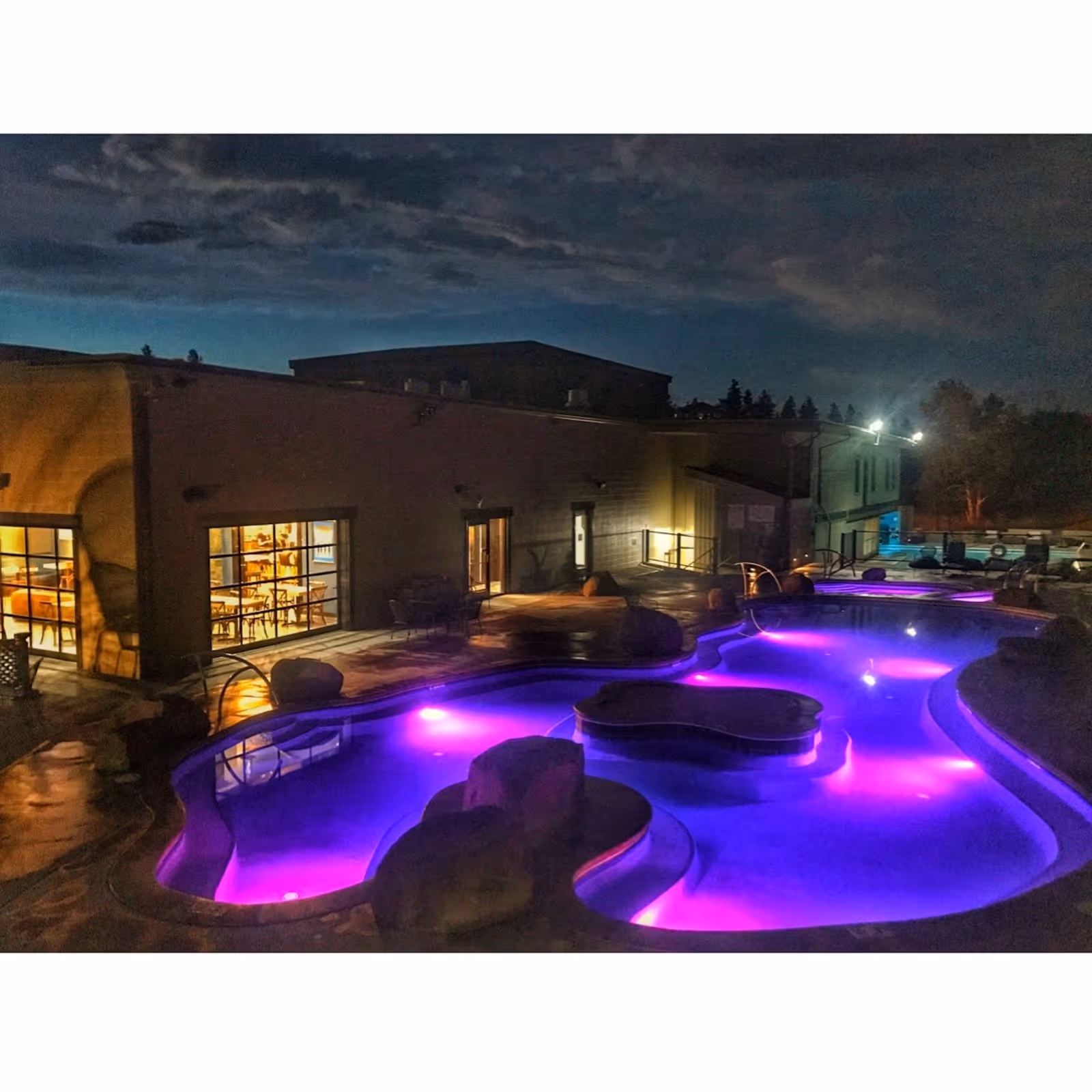 Night view of Broadwater Hot Springs outdoor pool lit with purple lights beside the building near Helena Montana.