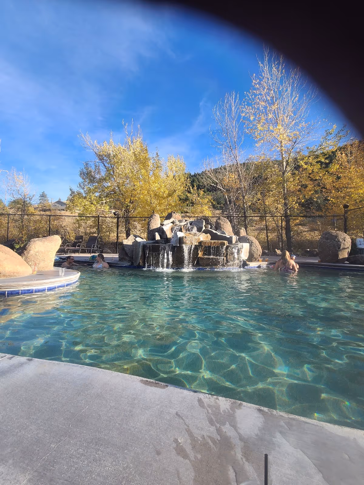 Wide outdoor mineral pool at Broadwater Hot Springs featuring a waterfall and autumn trees near Helena Montana.