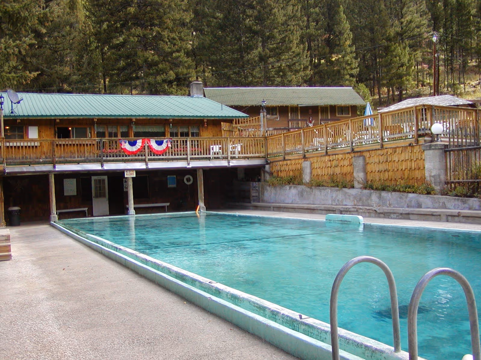 Large outdoor pool with clear water next to a wooden building and deck at Lost Trail Hot Springs near Sula Montana.