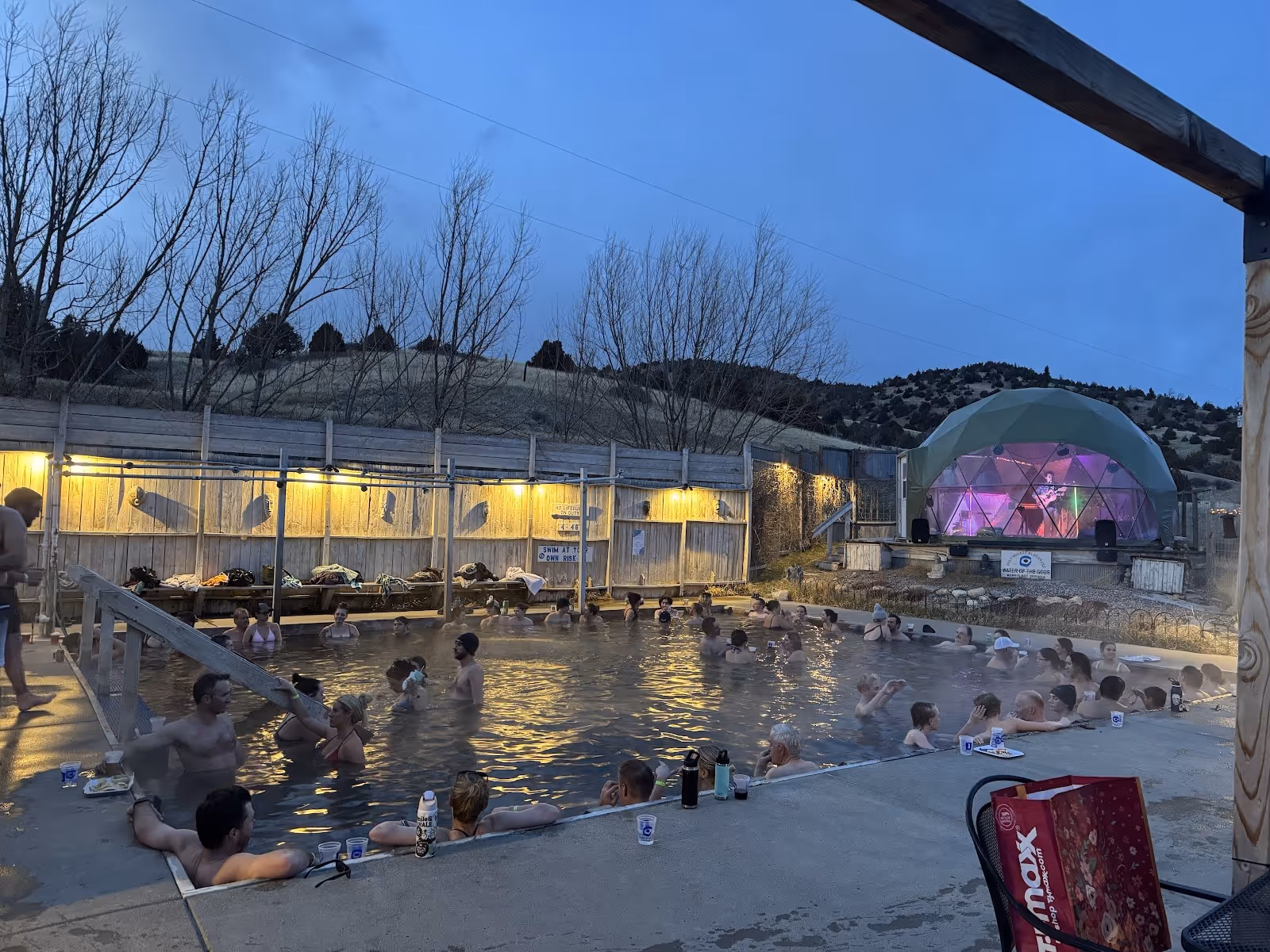 Norris Hot Springs outdoor pool at dusk filled with many people, steam rising and illuminated dome in the background near Norris Montana.
