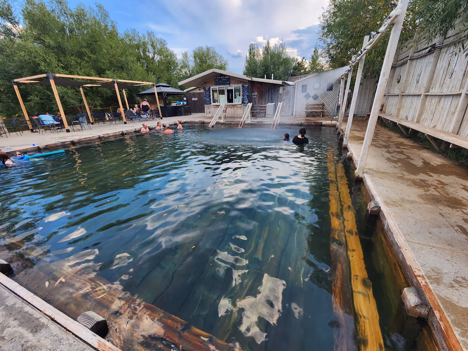 Indoor covered hot spring pool with clear water, wooden benches along walls, and bathers relaxing inside Norris Hot Springs Montana.
