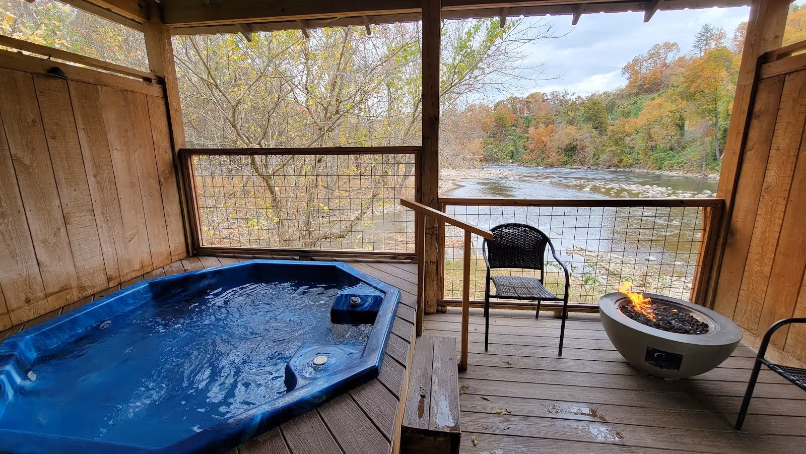 Blue outdoor spa pool on wooden deck overlooking a flowing river and autumn trees at Hot Springs Resort & Spa in Hot Springs, North Carolin.