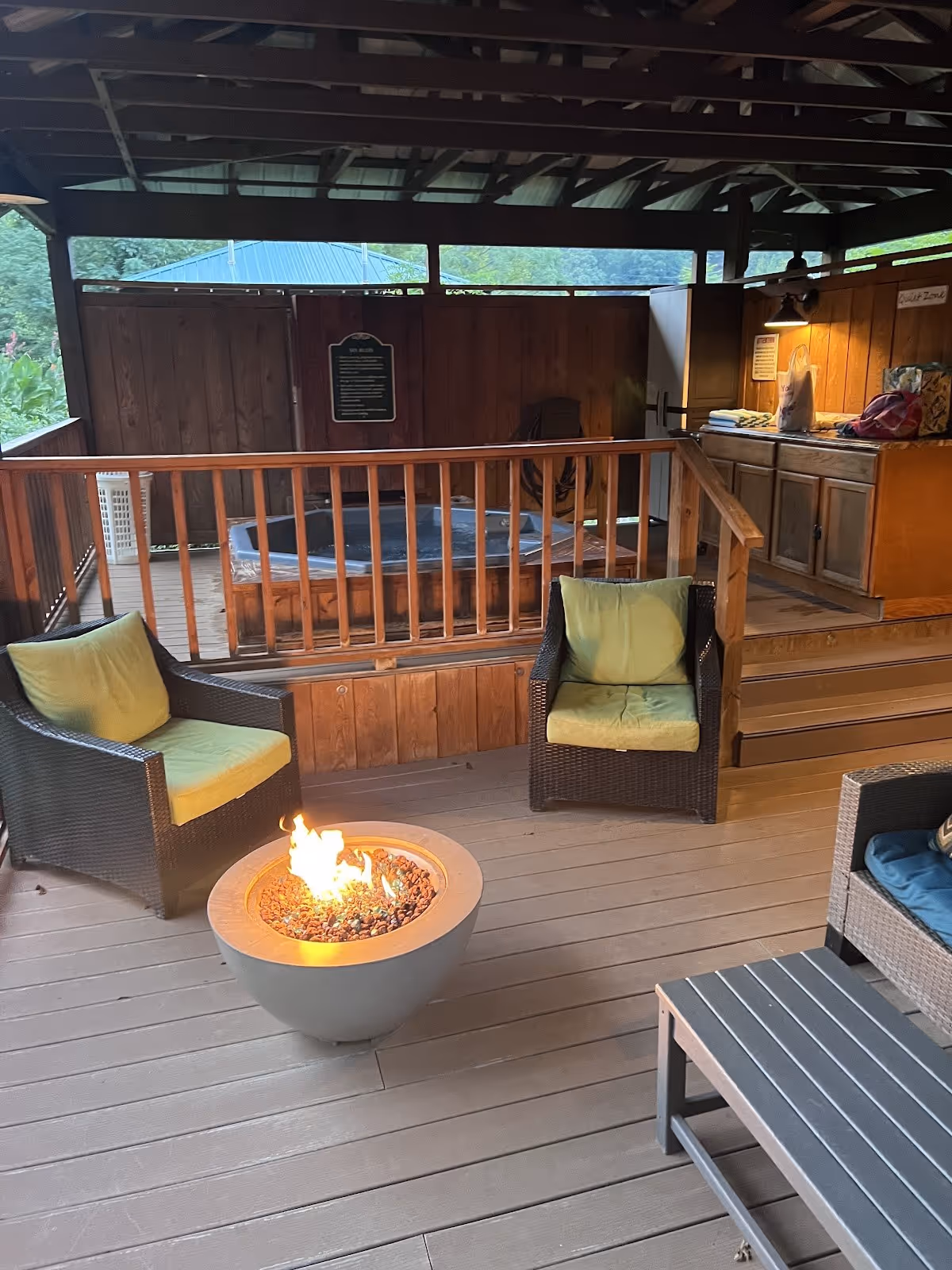 Covered outdoor seating area with green cushioned chairs around a fire pit, adjacent to a blue spa pool at Hot Springs Resort & Spa in Nort.