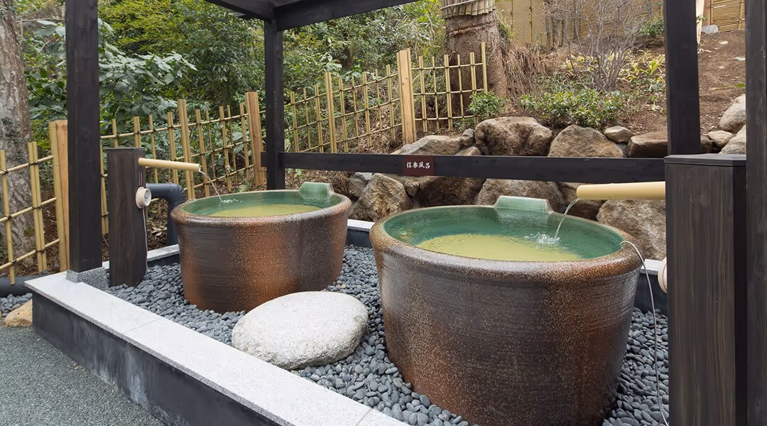 Pair of large ceramic soaking tubs filled with water and bamboo spouts in a landscaped area at Hakone Yuryo, Hakone.