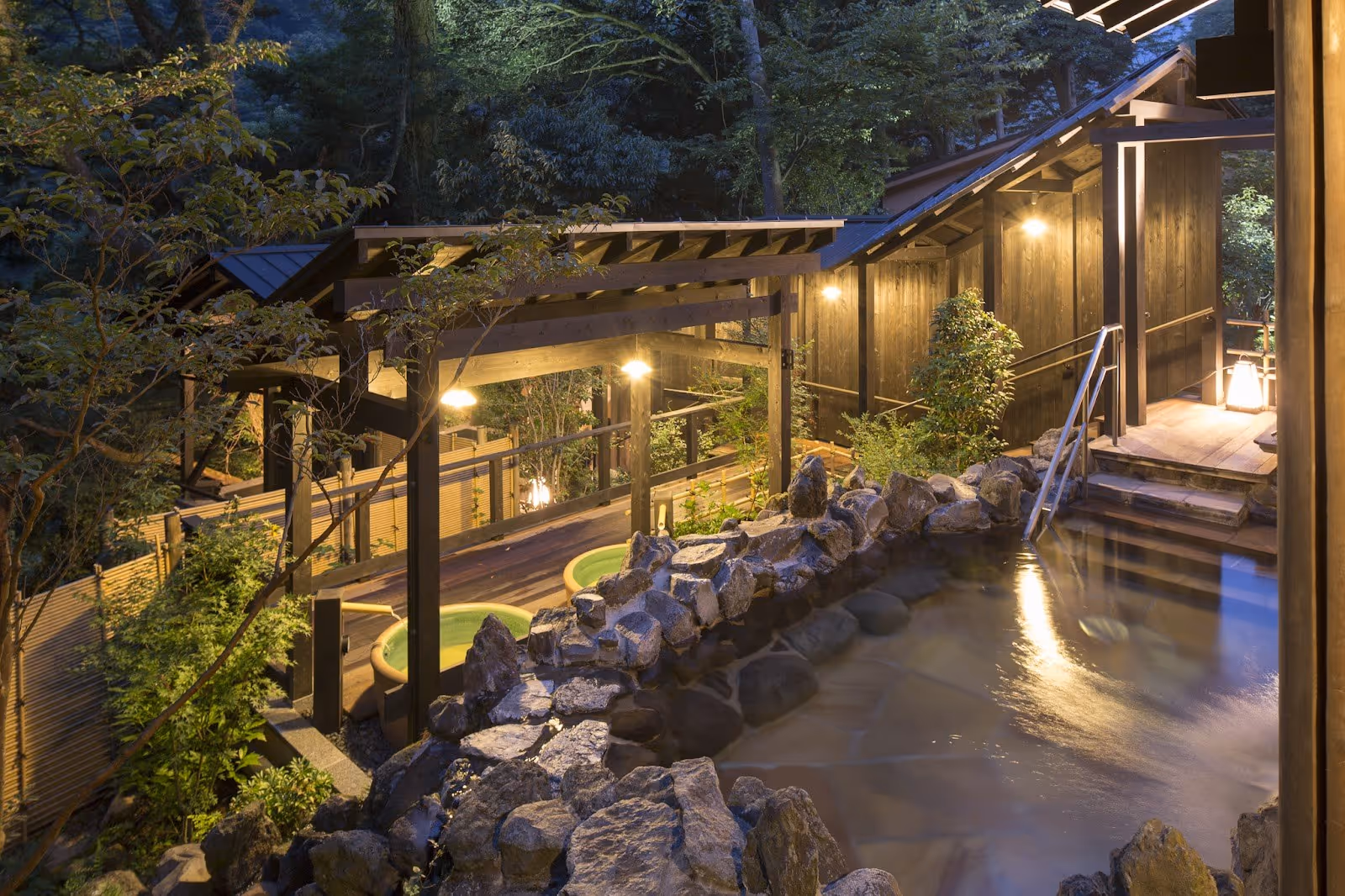 Outdoor hot spring pool at Hakone Yuryo surrounded by rock edges and lit wooden structures in Hakone, Japan.