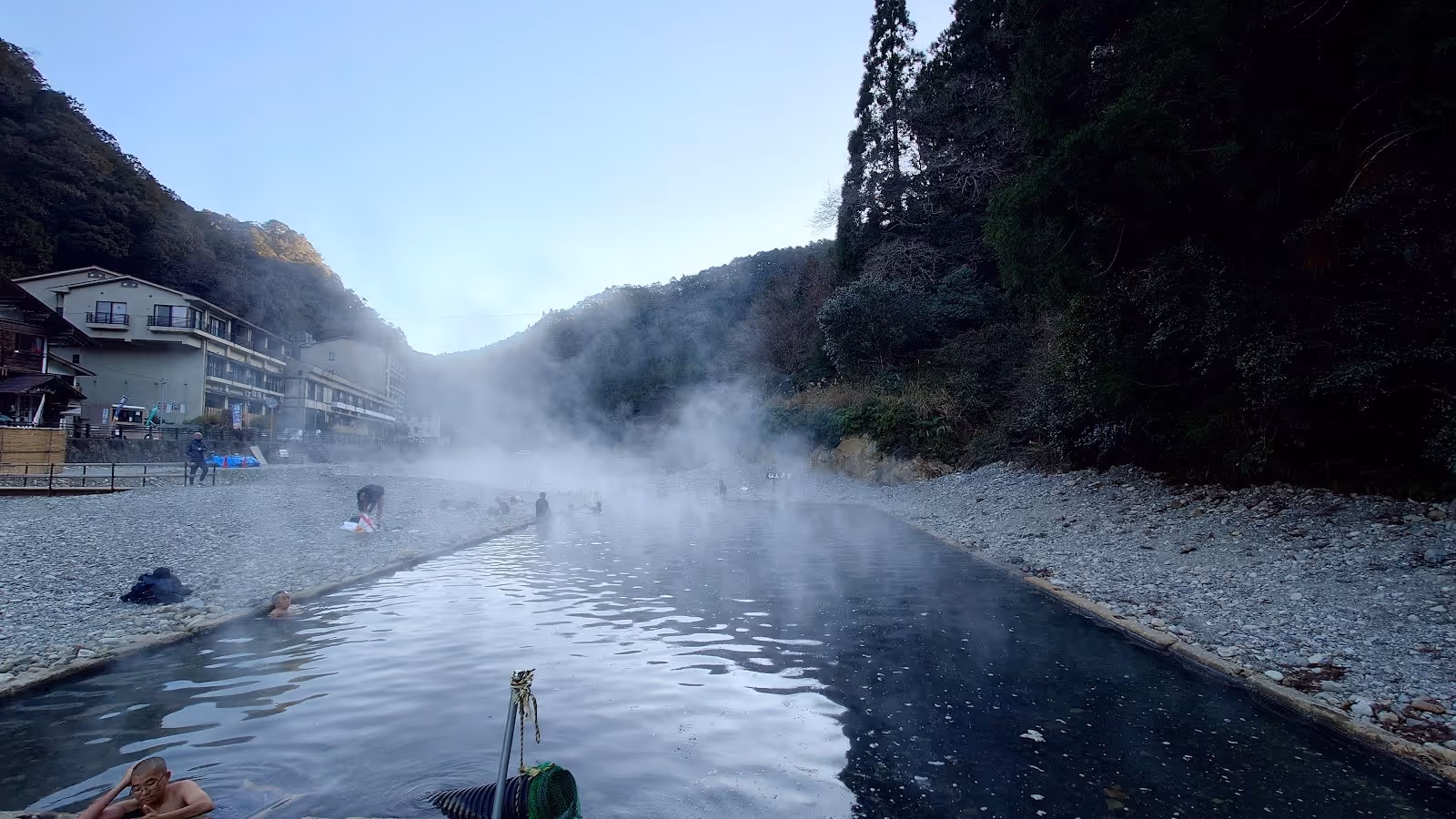 Long outdoor river bath with steam and people soaking beside pebble banks at Kawayu Onsen Sennin-buro near Tanabe city.