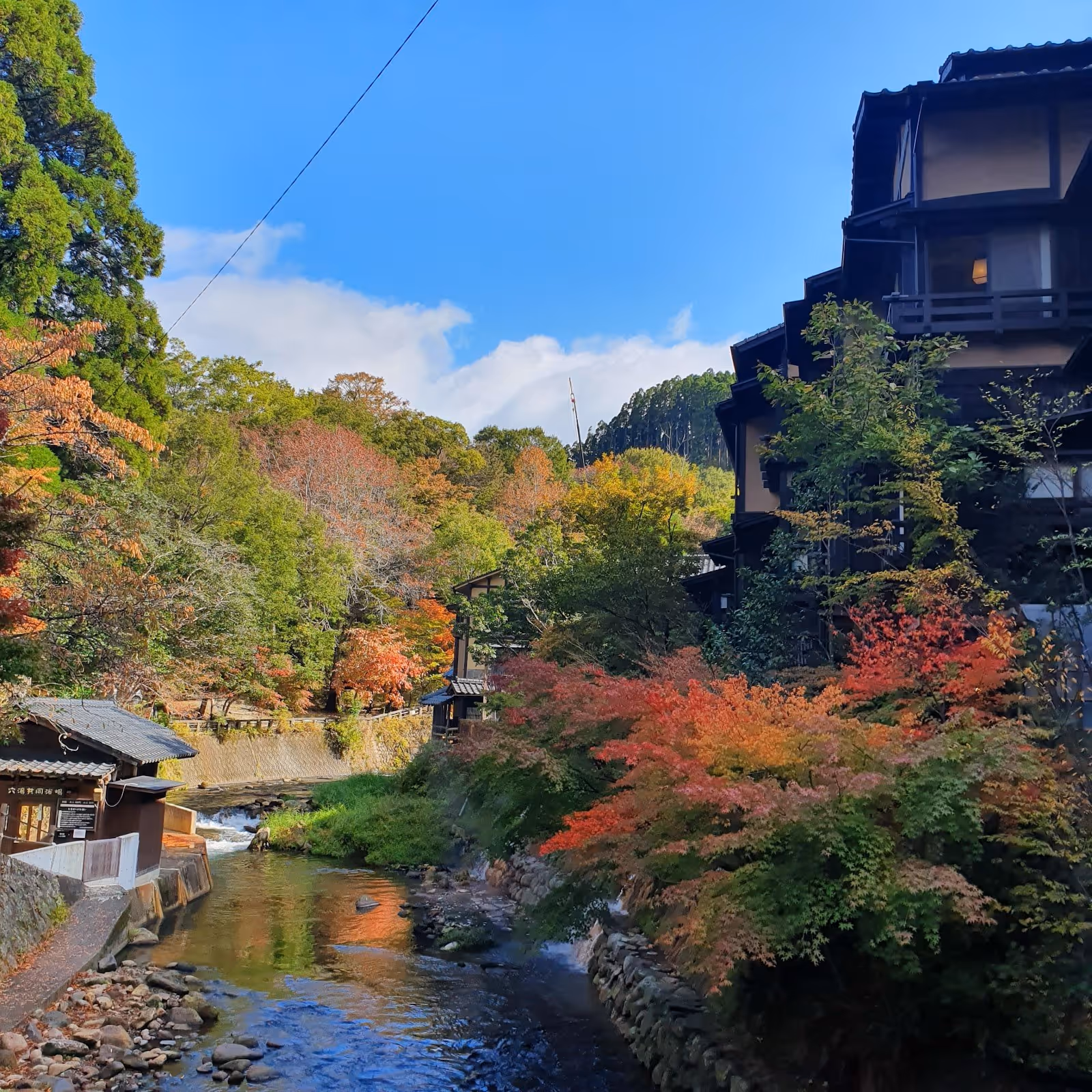 River flowing beside wooden buildings and trees with autumn leaves at Kurokawa Onsen in Minamioguni, Japan.
