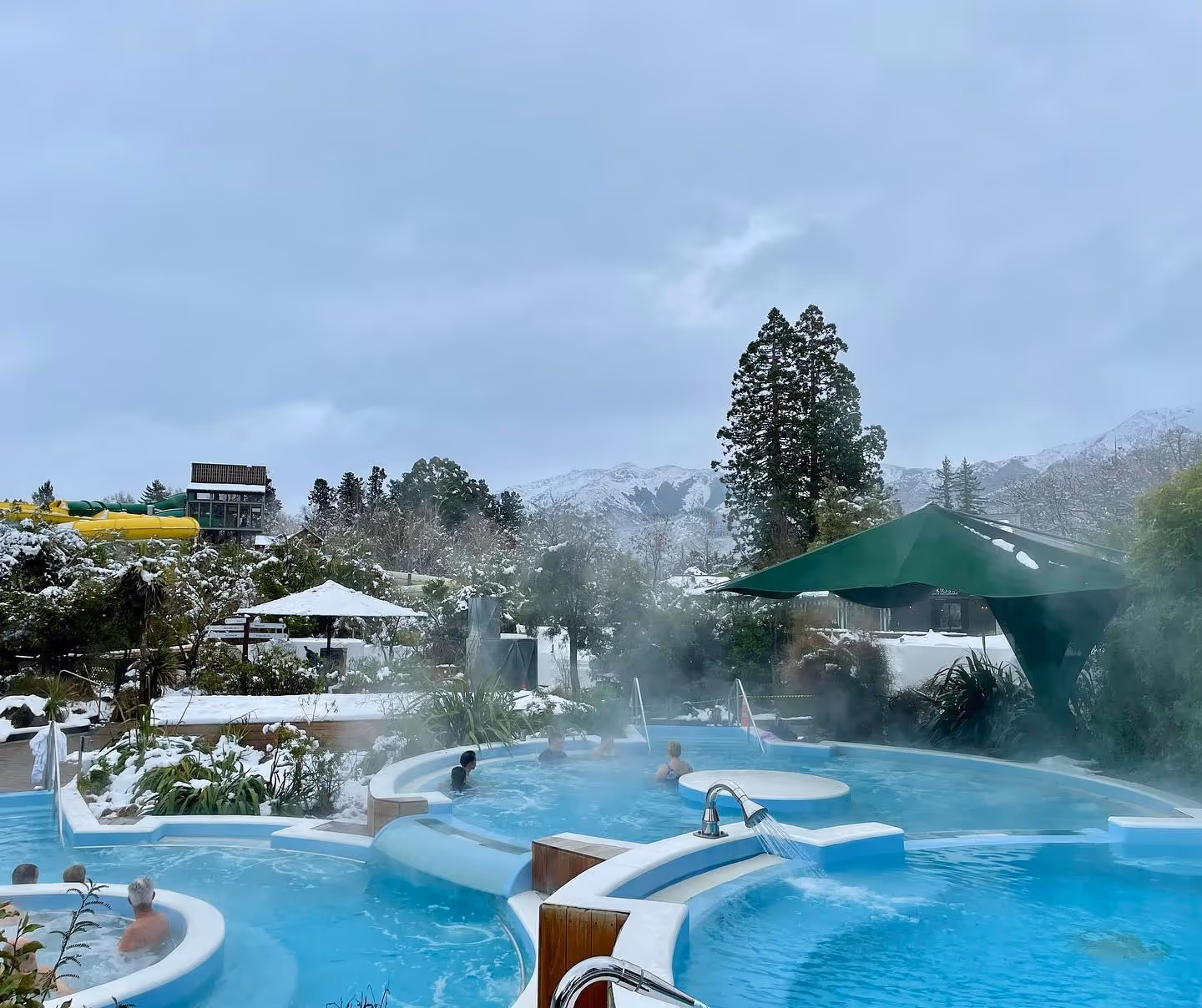 Hanmer Springs Thermal Pools & Spa features multiple steaming hot spring pools with snow-capped mountains in the background near Hanmer Spr.