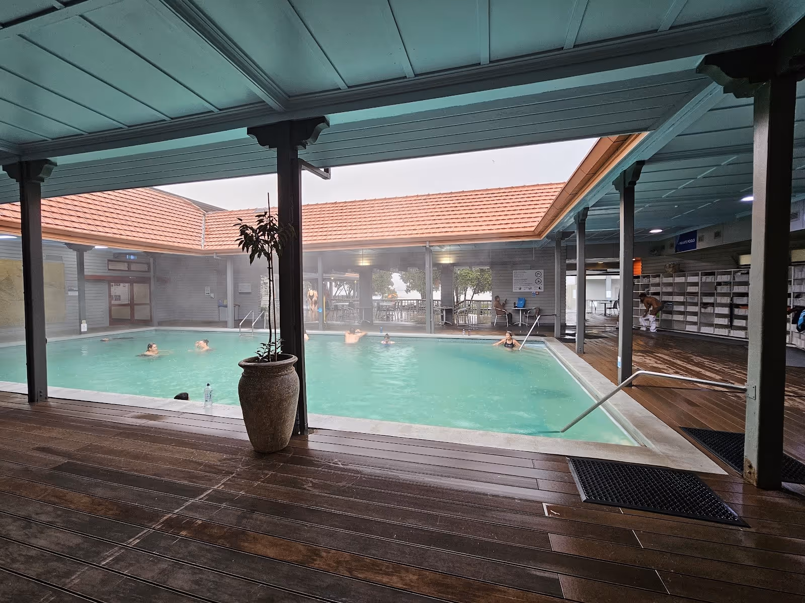 Indoor hot spring pool with pale green water and steam rising under a covered open roof structure with wooden floors at Polynesian Spa.