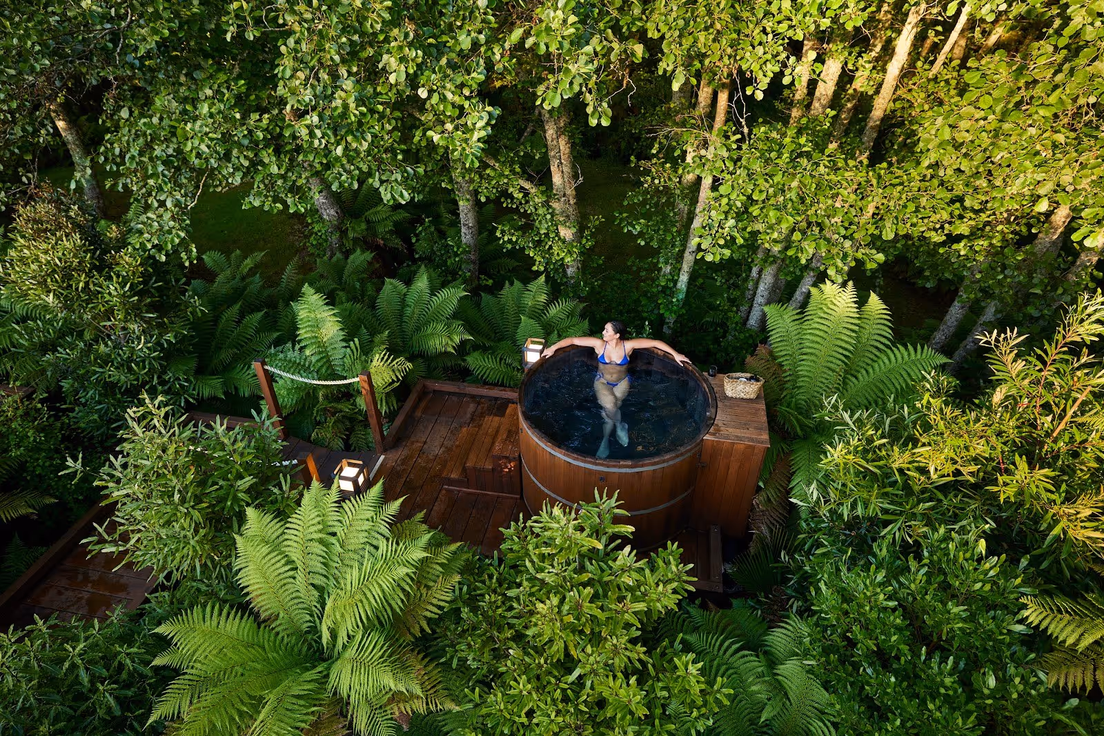 Woman relaxing in a round wooden hot tub surrounded by lush green trees and ferns at Secret Spot Hot Tubs near Rotorua New Zealand.