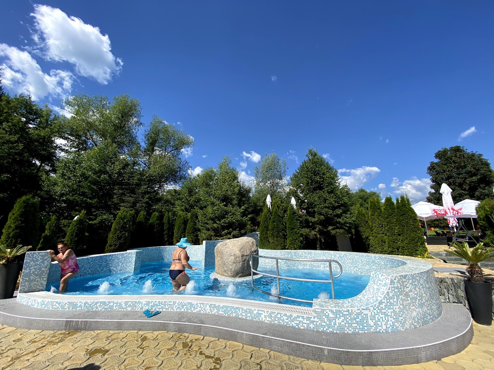 Two women enjoying a small curved pool with a large rock feature and bubbling water at Alpha Spa & Pool in Dobrinishte.