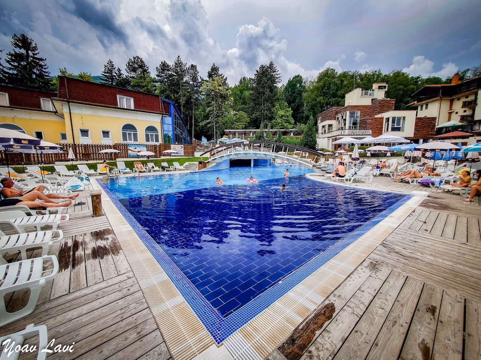 Outdoor spa pool at Aqua Club Kotvata in Sapareva Banya Bulgaria with blue water and people swimming under cloudy sky.
