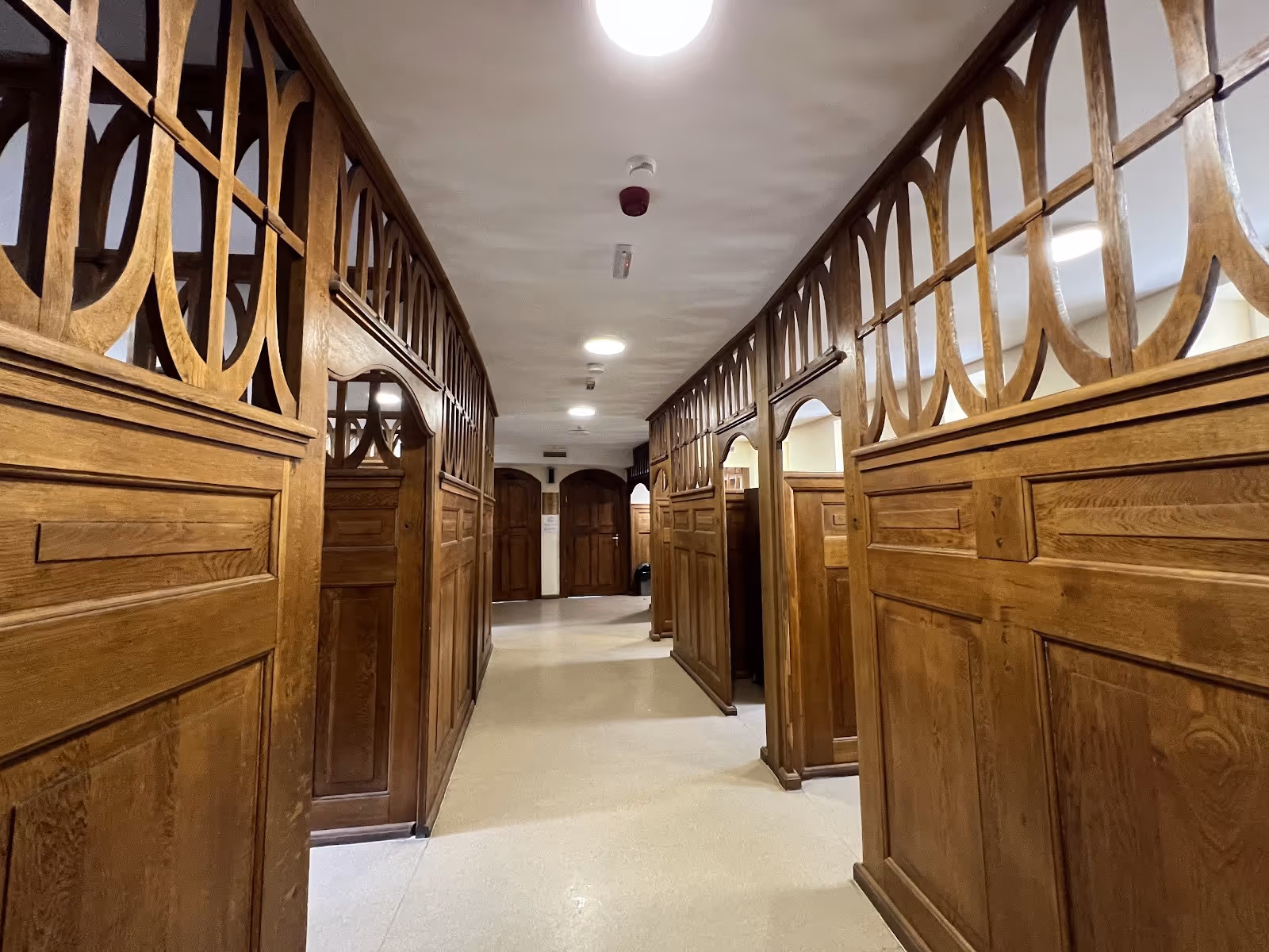 Hallway with wood paneled walls and doors, overhead lights, and cream flooring leading to separate bathing areas at the hot springs in Bank.