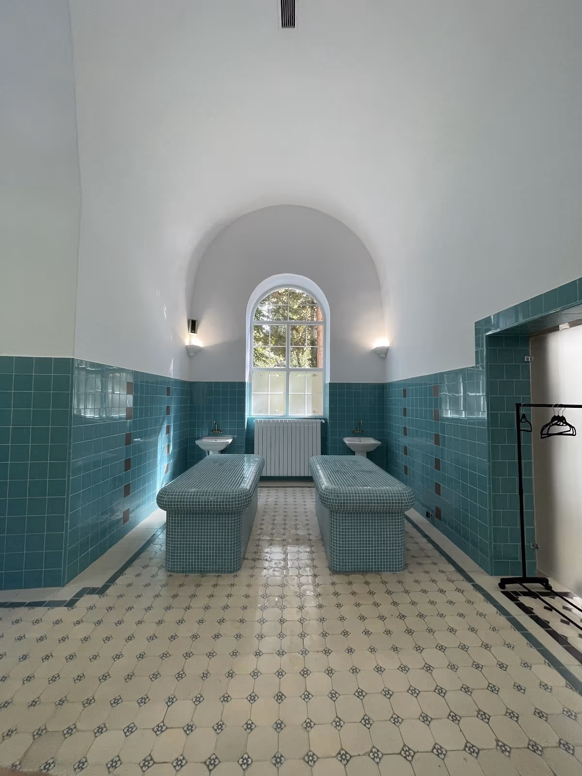 Spacious spa treatment room with teal mosaic benches, patterned floor tiles, and an arched window letting in natural light at Bankya Bulgar.