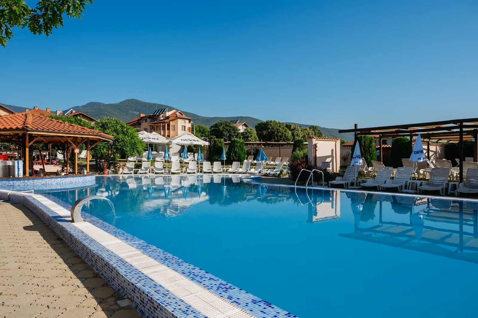 Outdoor spa pool with clear blue water and many white lounge chairs under umbrellas in Velingrad, Bulgaria.