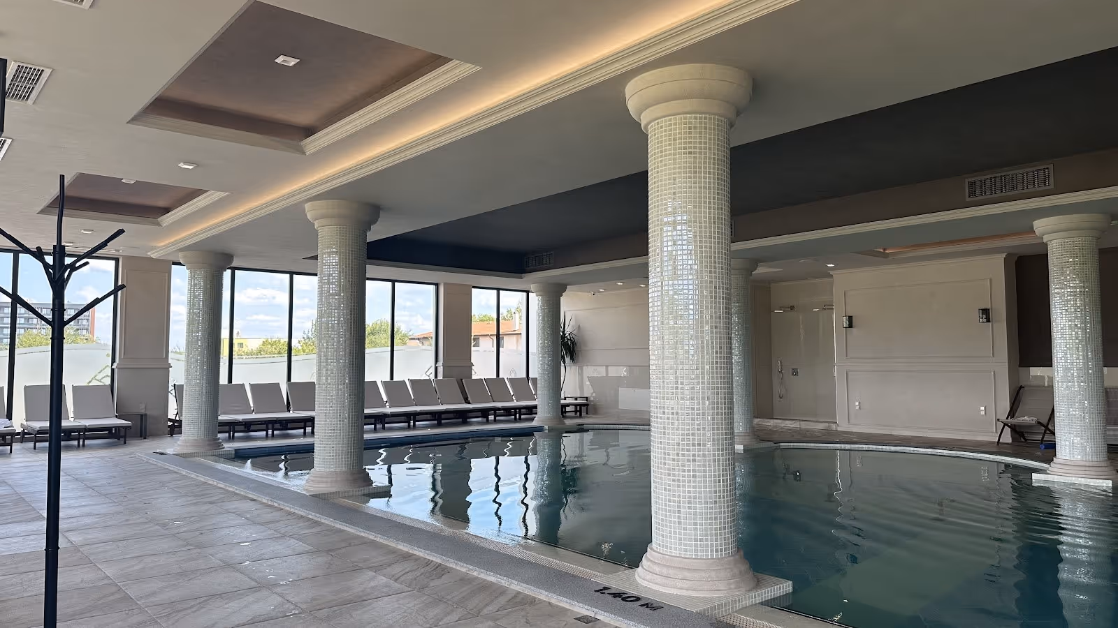 Indoor hot spring pool at Grand Resort Pavel Banya Mineral Pools in Pavel Banya Bulgaria with tiled columns and lounge chairs by windows.