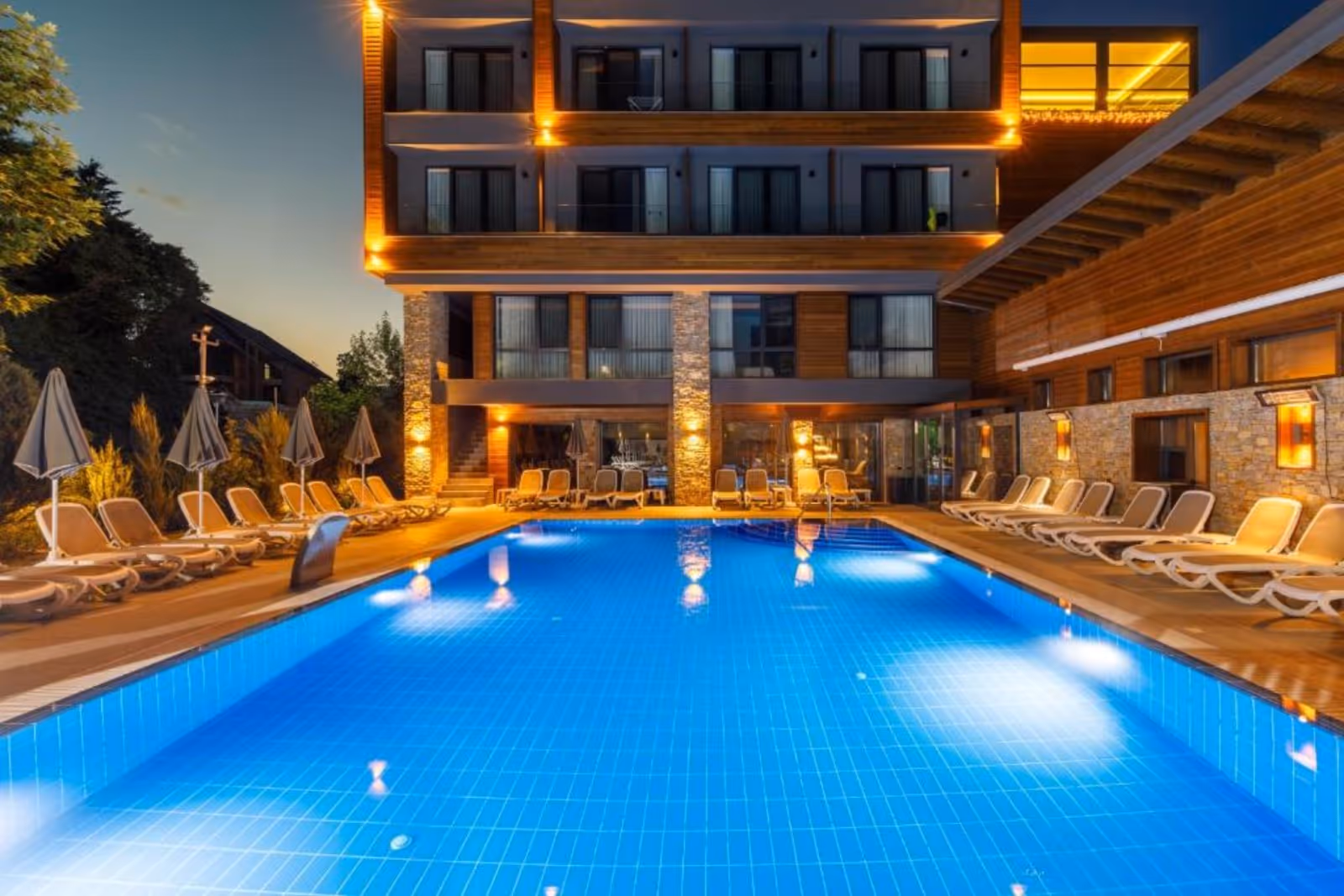Night view of Regnum Banya Thermal Pools outdoor pool with clear blue water and empty lounge chairs in Banya, Bulgaria.