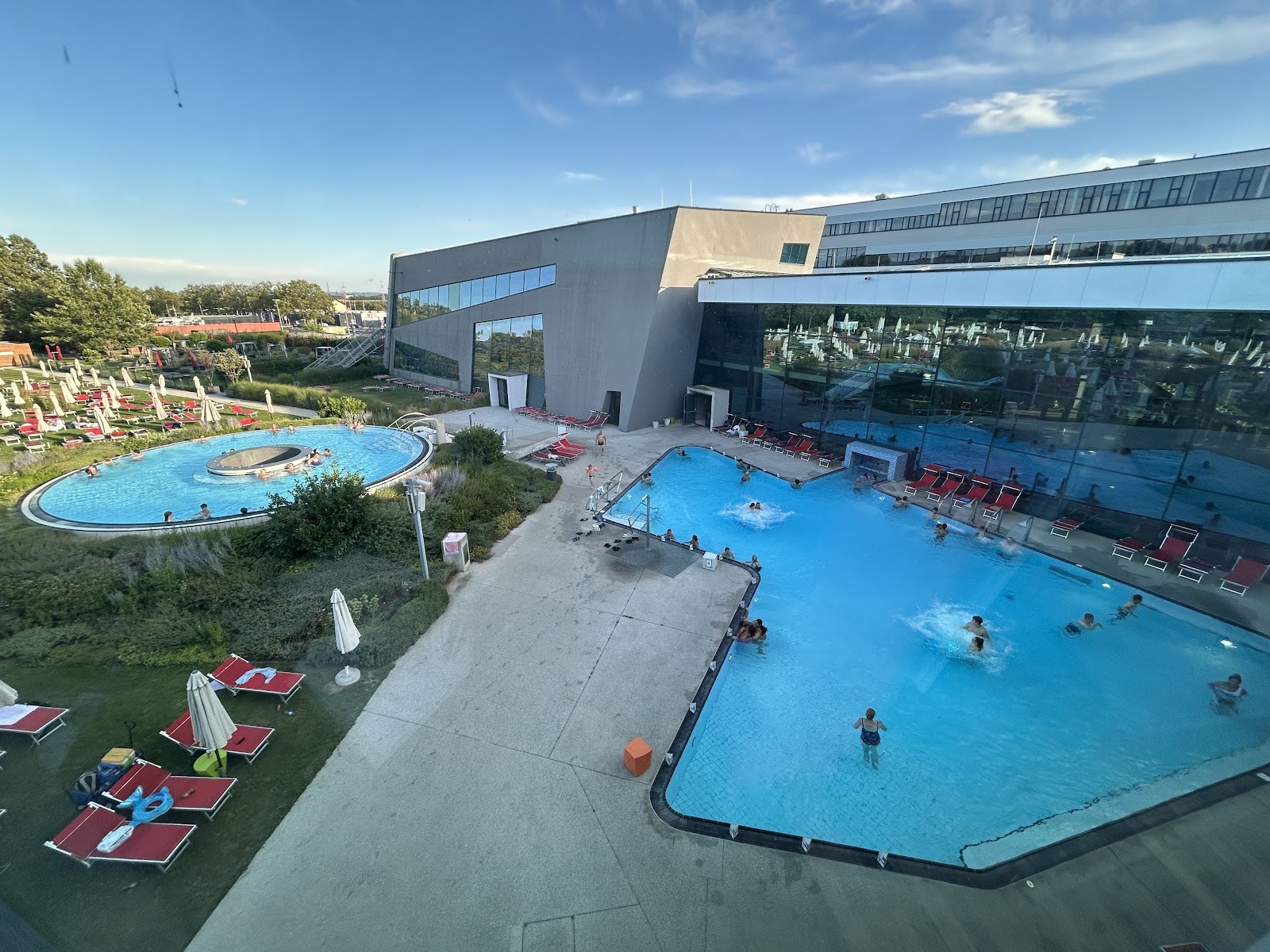 Outdoor hot spring pools at Therme Wien in Vienna Austria with a large circular pool and a rectangular pool beside a modern building.