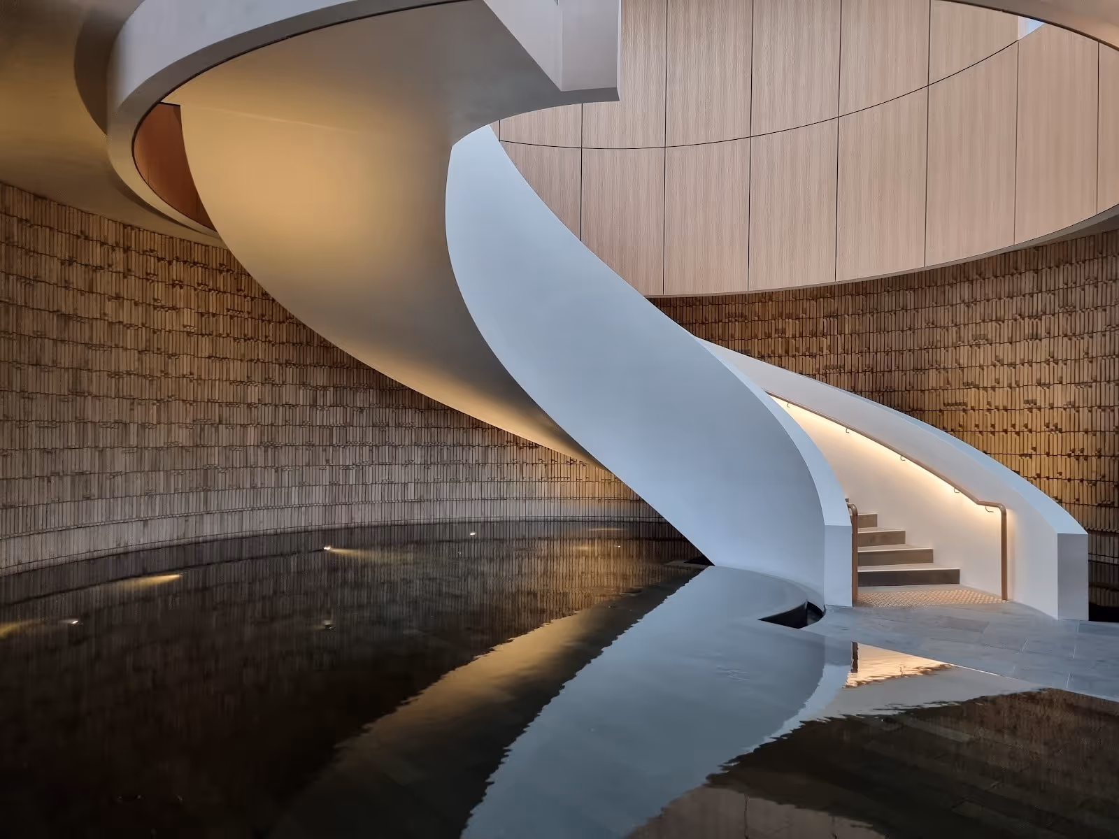 Indoor spa pool reflecting a modern white spiral staircase and wood-paneled walls inside Alba Thermal Springs spa in Australia.