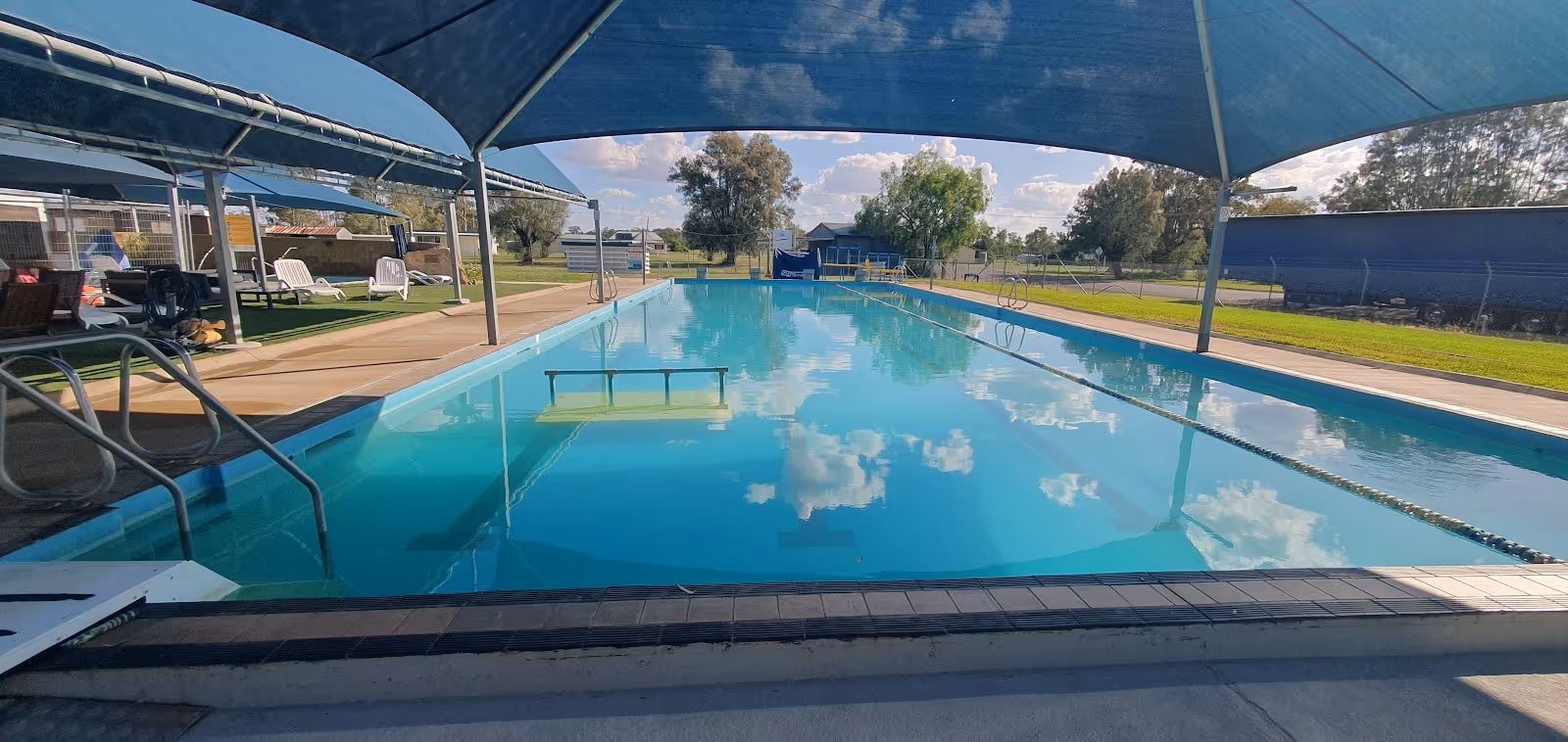 Large rectangular soaking pool at Boomi Artesian Spa Pools with clear blue water and shade structures along the poolside.