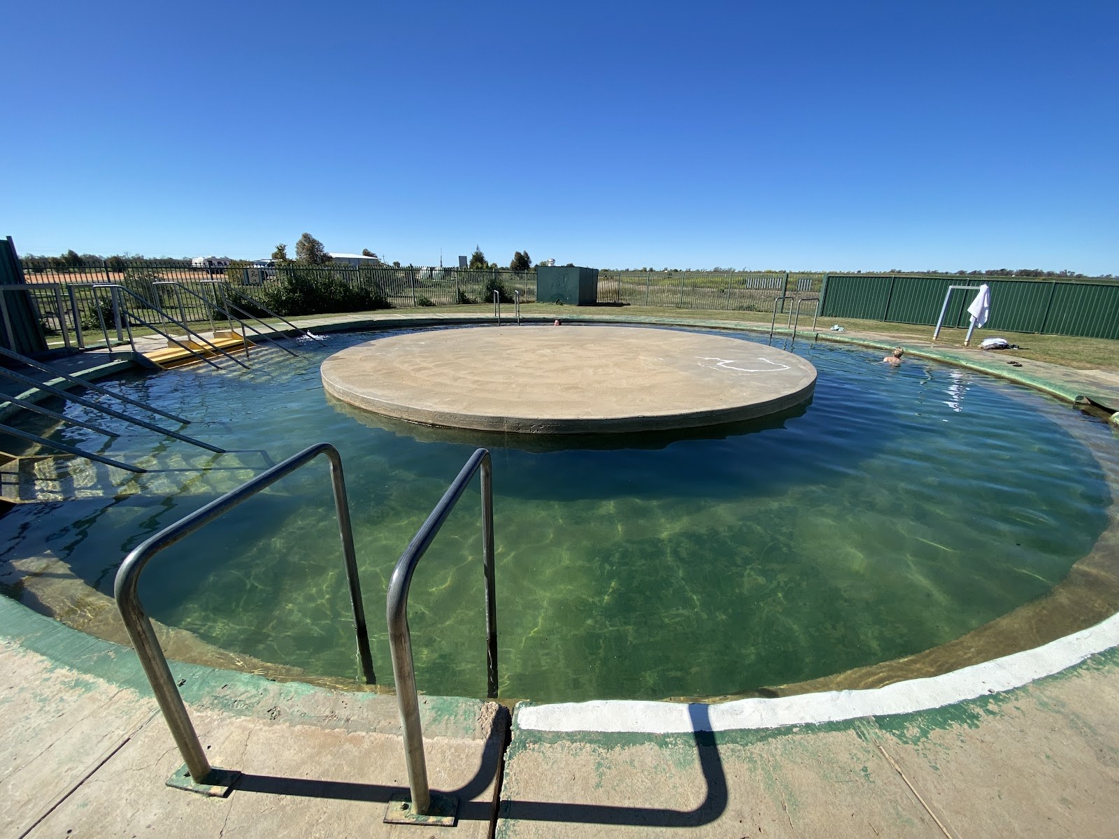Circular outdoor hot spring pool with clear water and metal handrails under a clear blue sky at Burren Junction Artesian Bore Baths in Burr.