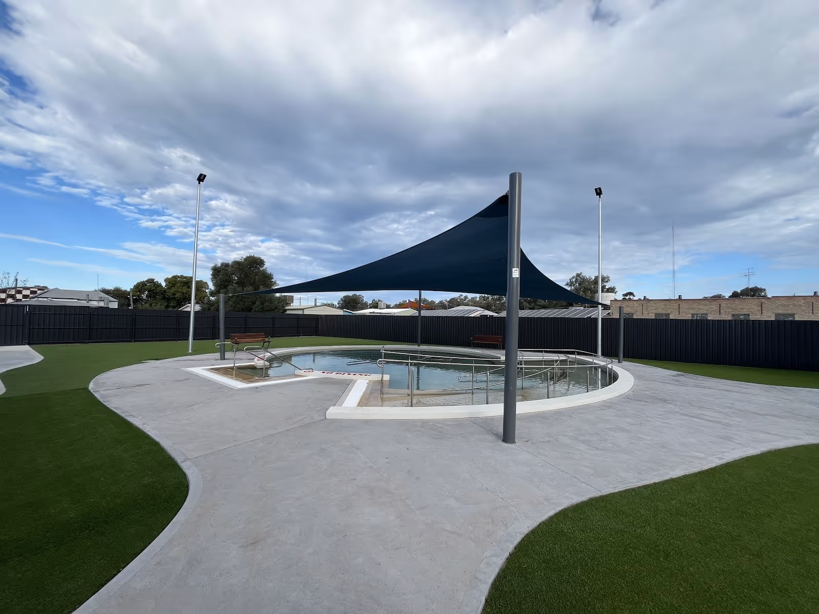 Collarenebri Bore Bath outdoor pool under dark shade sail on cloudy day with paved surround and artificial grass in New South Wales.