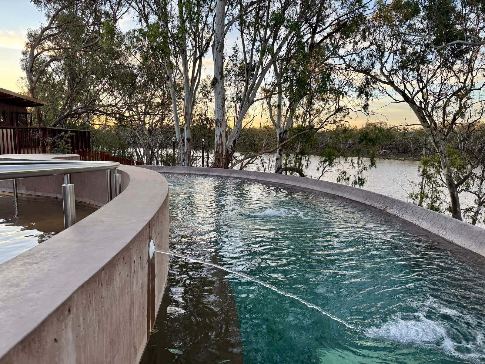 Curved concrete outdoor spa pools with clear water flowing from a spout near river trees at Cunnamulla Hot Springs in Queensland Australia.