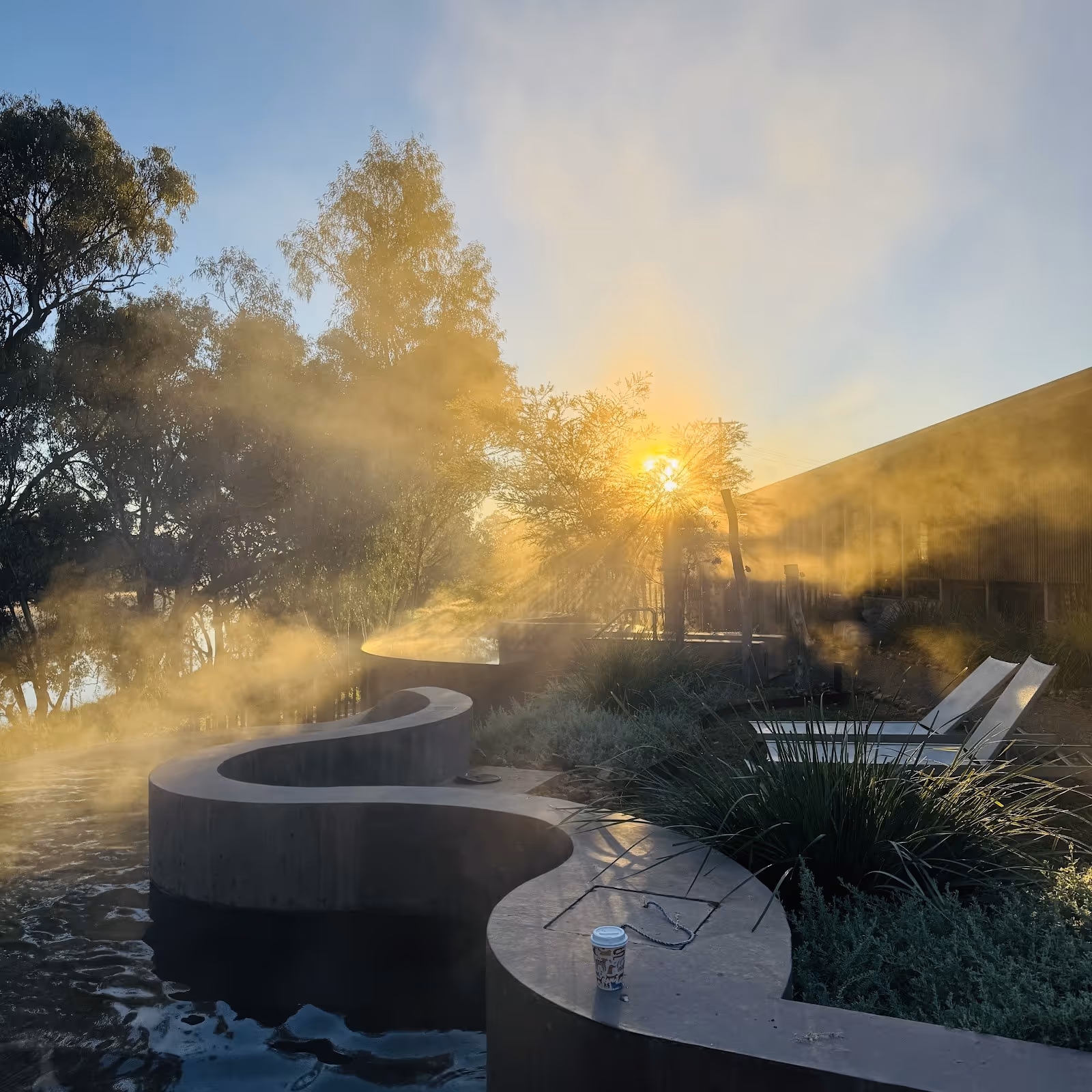 Indoor hot spring soaking pool with white tiles and stone flooring beneath a round skylight allowing natural sunlight in at Cunnamulla Hot.