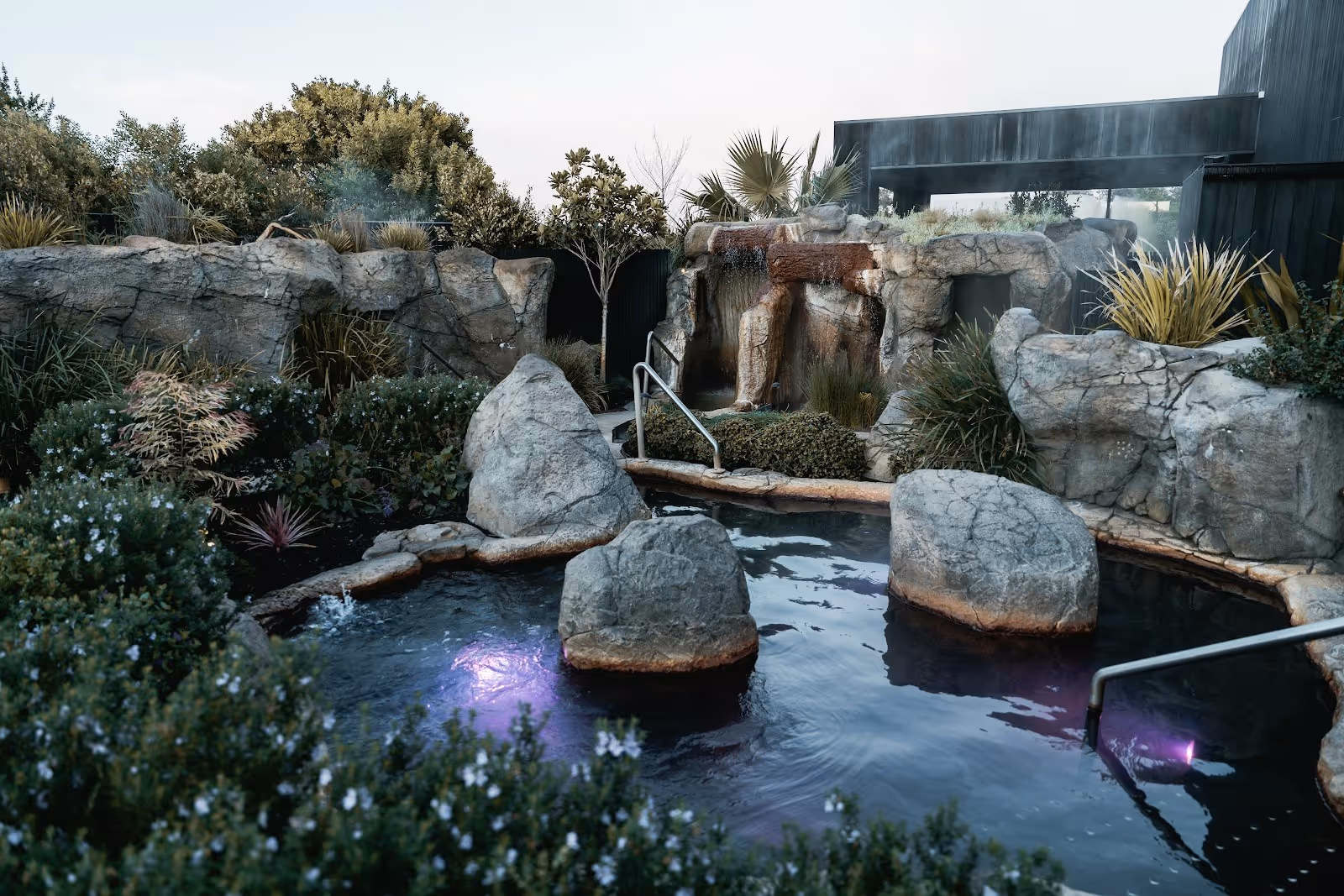Outdoor hot spring pool at Deep Blue Hot Springs with rocks, garden plants, steam, and purple underwater lights near Warrnambool Australia.