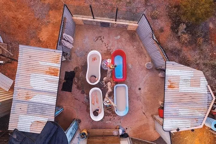 Aerial view of outdoor bathing area with four clawfoot tubs filled with water and people soaking at Eulo Artesian Mud Baths Australia.