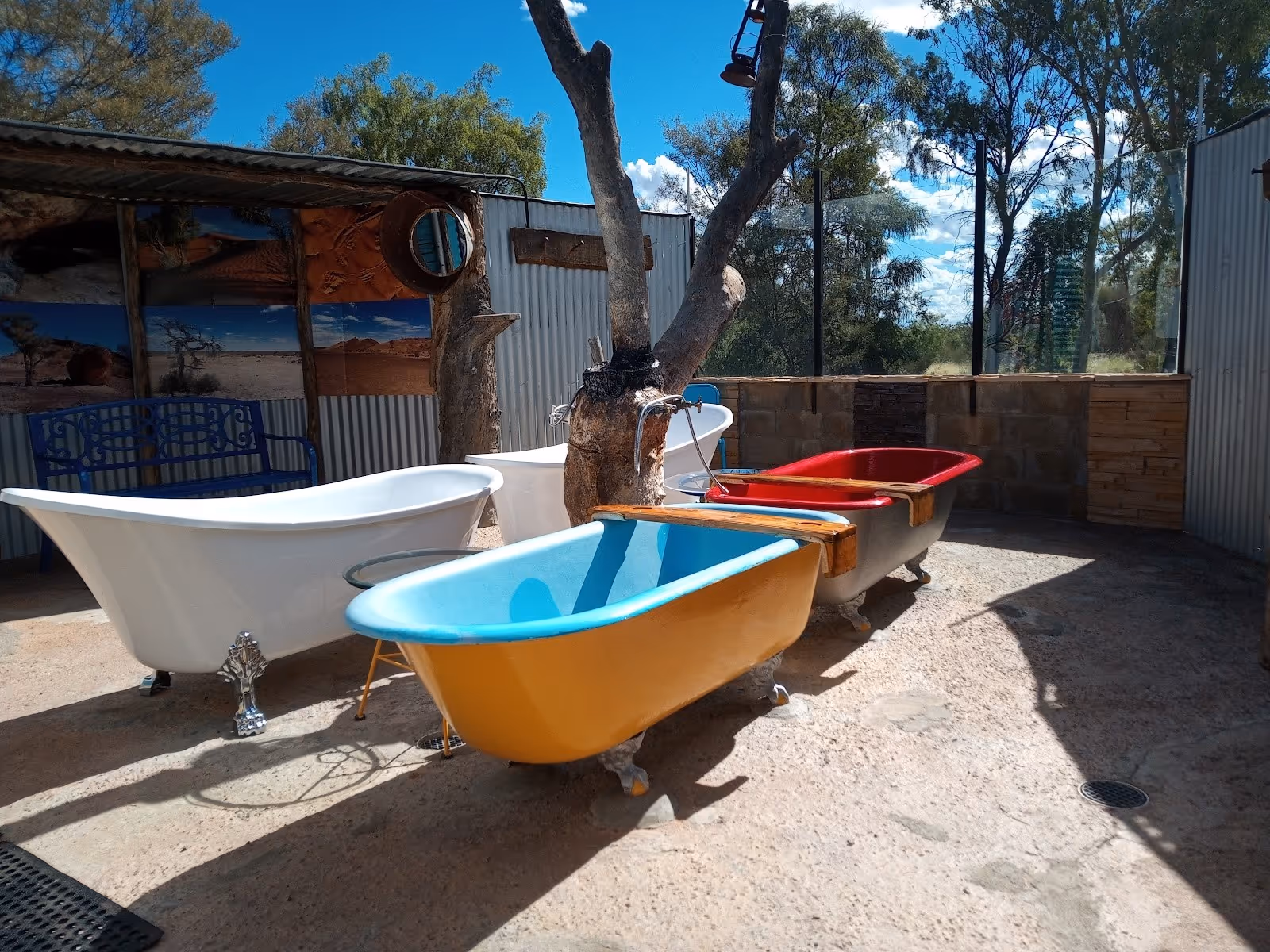 Outdoor area with several empty colorful clawfoot tubs and corrugated metal walls under a clear blue sky at Eulo Artesian Mud Baths.