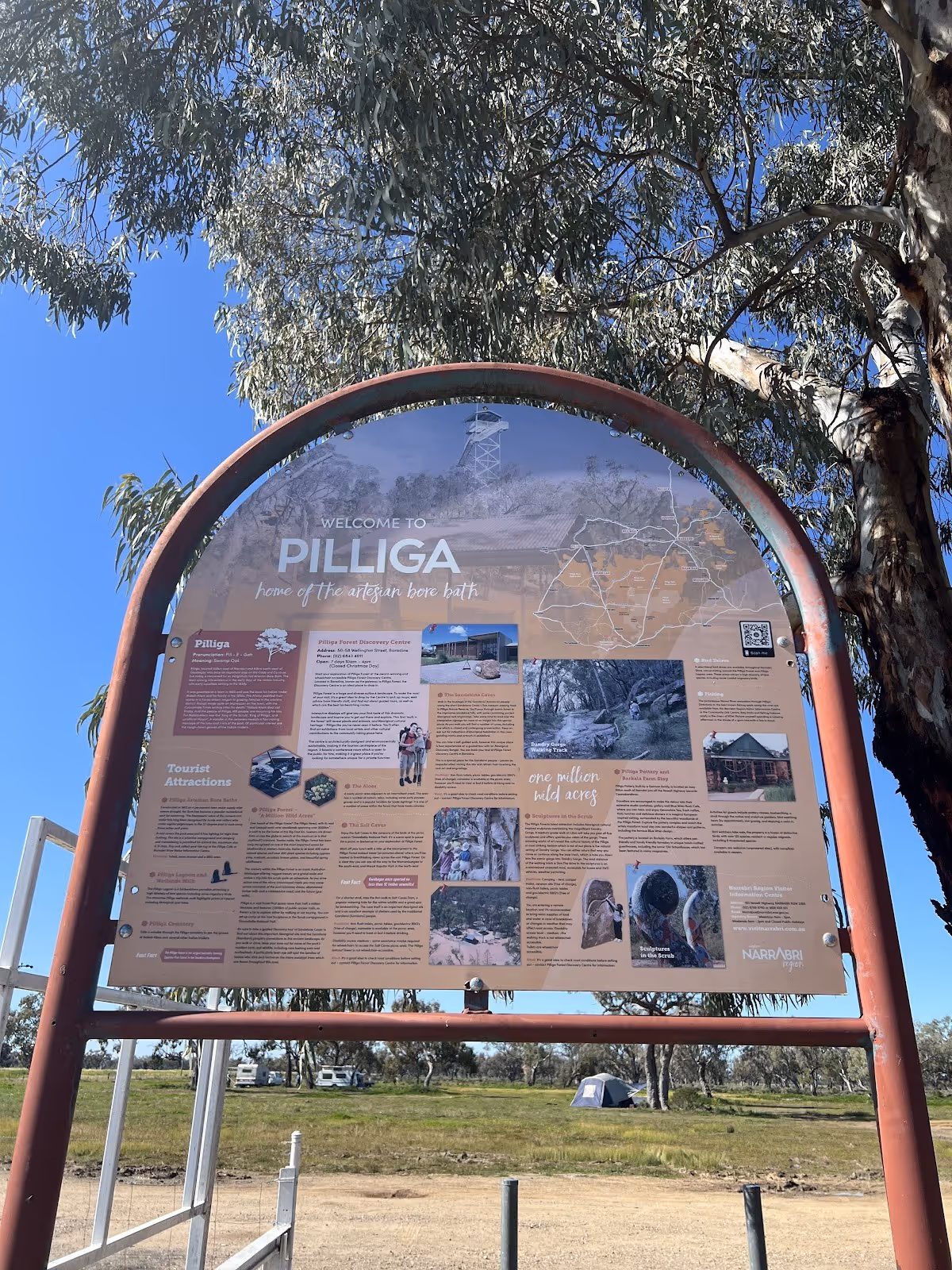 Information board welcoming visitors to Pilliga, highlighting the artesian bore baths and nearby attractions under a clear blue sky.