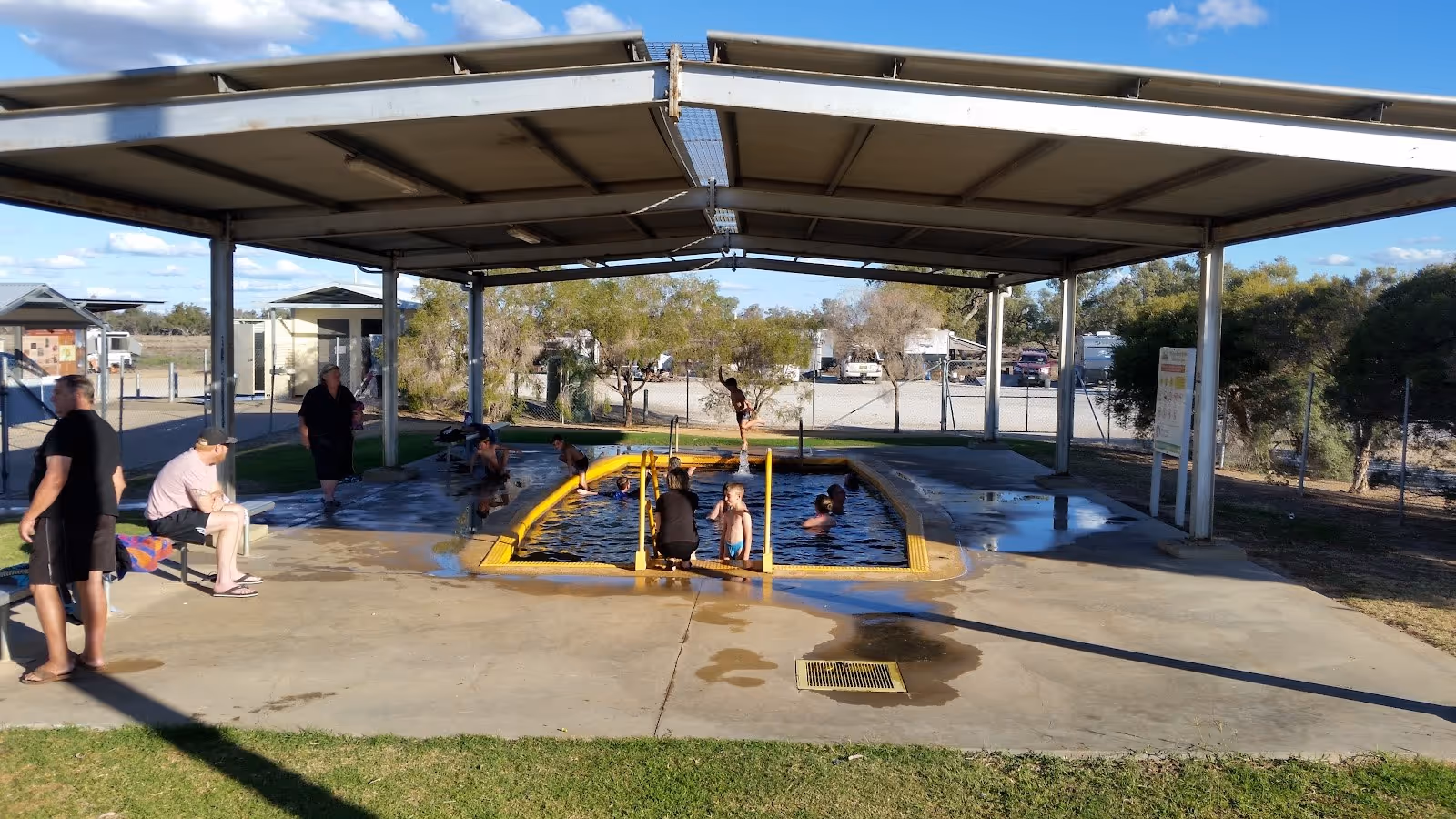 Sunny covered hot spring pool showing multiple visitors soaking and sitting around the concrete area at Pilliga Artesian Bore Baths near Na.