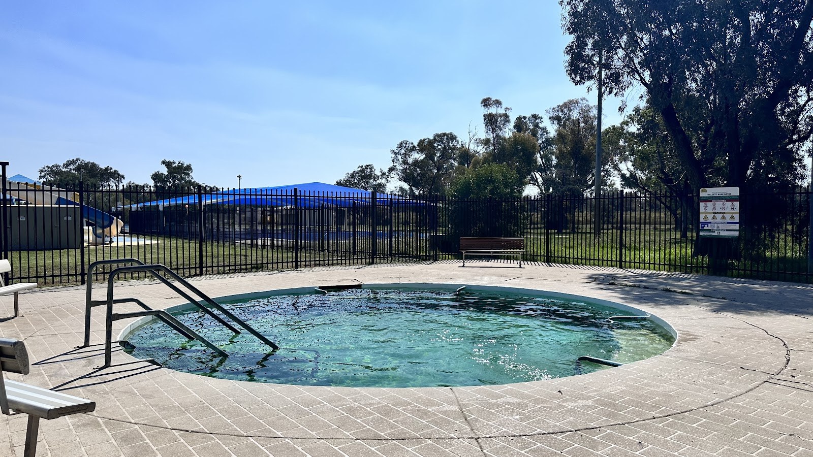 Round outdoor pool with clear water at Walgett Artesian Bore Baths, surrounded by metal fence and leafy trees in Walgett, New South Wales.