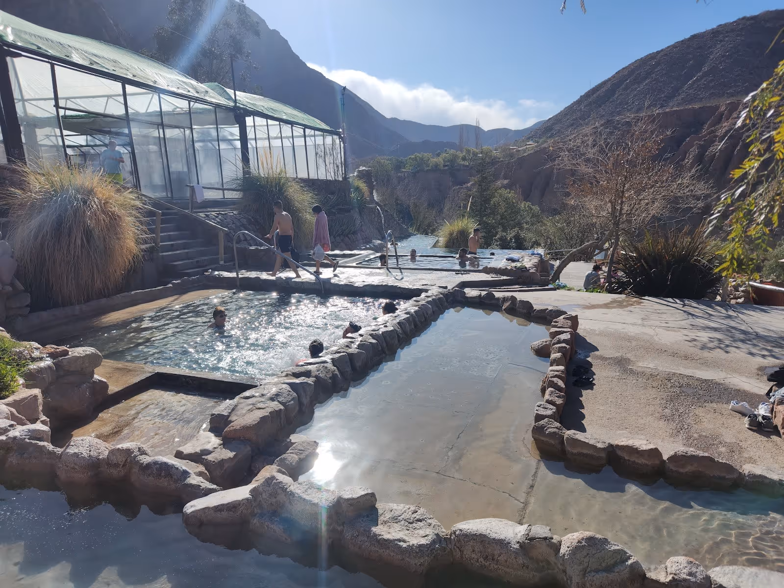 Multiple outdoor hot spring pools with stone edges at Termas de Cacheuta near Mendoza, Argentina under a clear sky with mountain views.