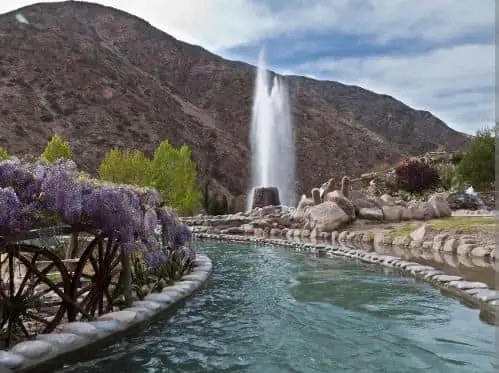 Narrow hot spring pool with fountain at Termas de Cacheuta set against mountain cliffs near Mendoza, Argentina with surrounding vegetation.