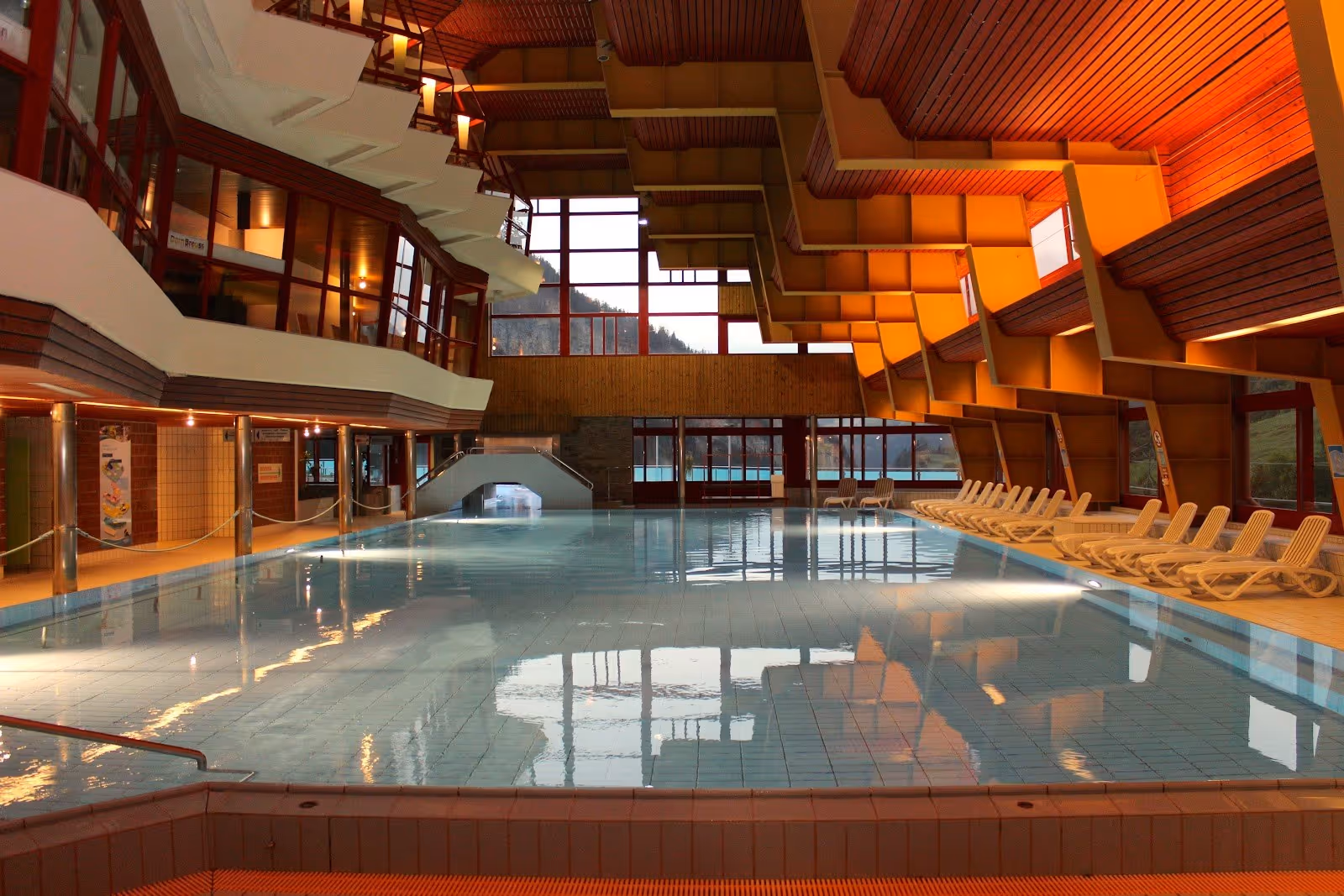 Indoor hot spring pool at Leukerbad Therme with rows of empty lounge chairs and warm wood paneling on the ceiling in Leukerbad Switzerland.