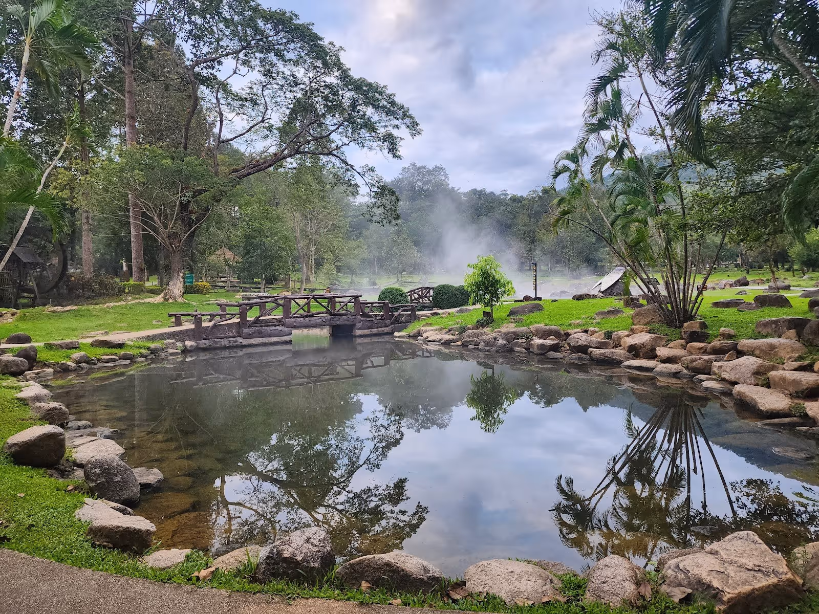 Natural outdoor hot spring pool surrounded by lush green trees and steam rising from the water near Lampang, Nan, Thailand.