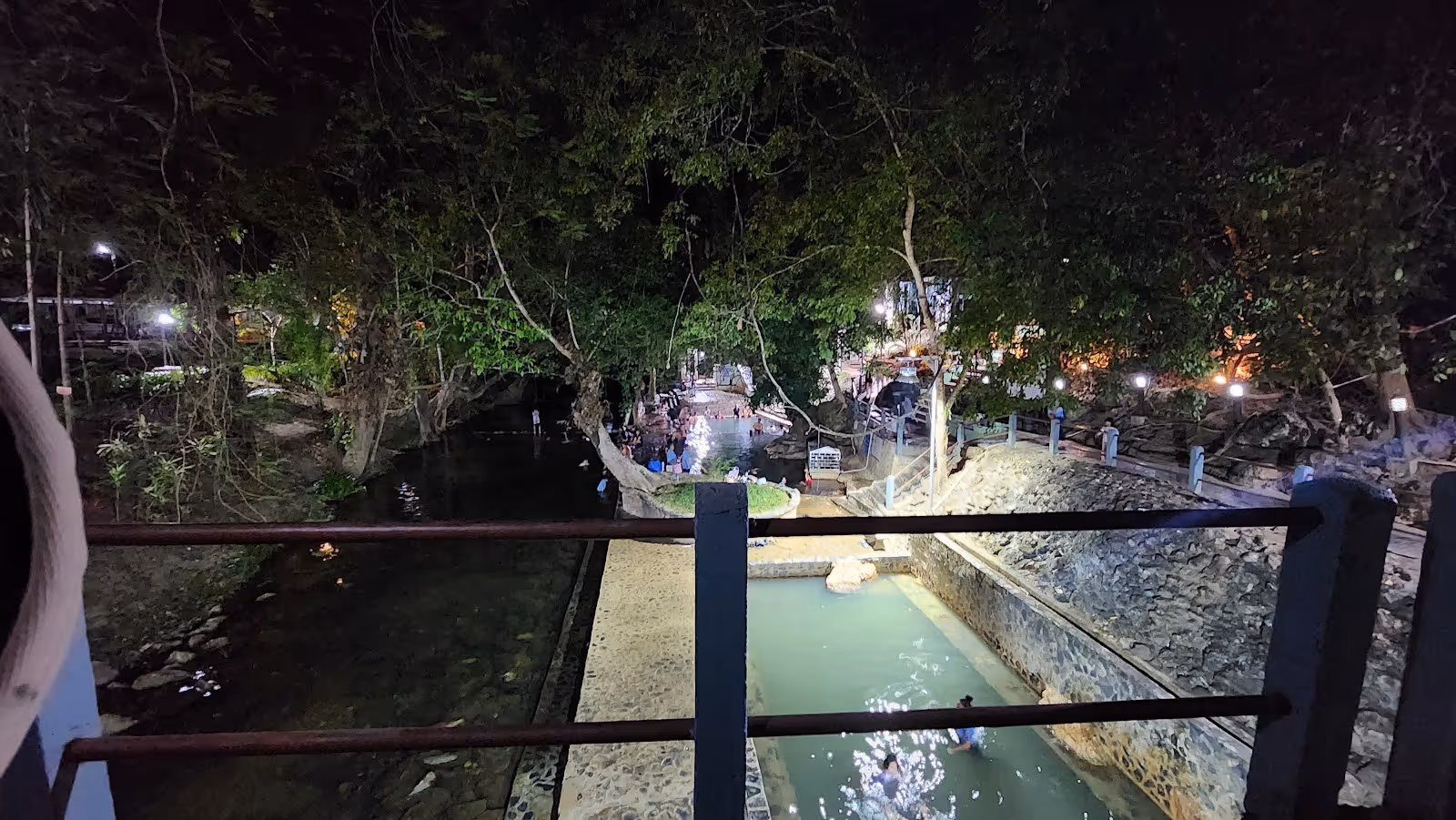Night view of illuminated hot spring pools with visitors at Hin Dad Hot Spring in Thong Pha Phum, Thailand.
