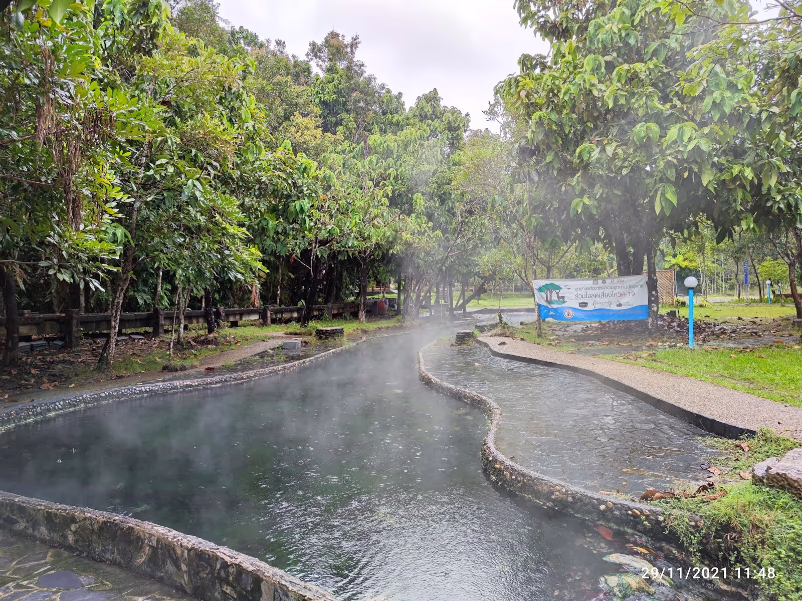 A steaming outdoor hot spring pool with curved edges surrounded by green trees at Kantang Hot Spring Forest Park near Trang, Thailand.