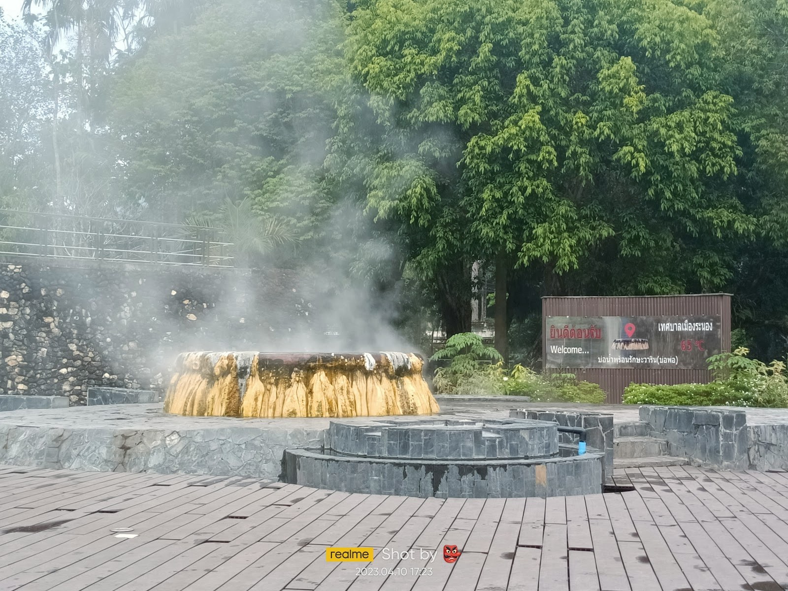 Steaming stone hot spring pool with mineral crust and surrounding trees in the park area of Raksawarin Hot Springs, Nan, Thailand.