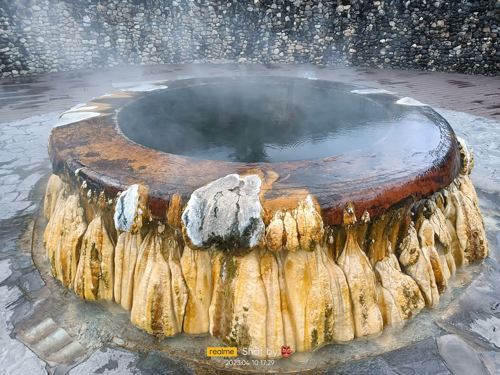 Circular hot spring pool with steaming water surrounded by mineral deposits at Raksawarin Hot Springs near Ranong, Thailand.